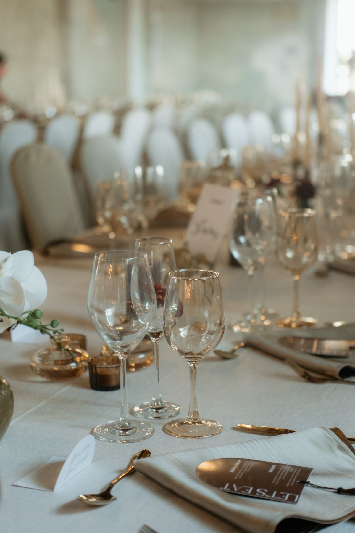 Elegant wedding reception table with gold glassware and white orchids.