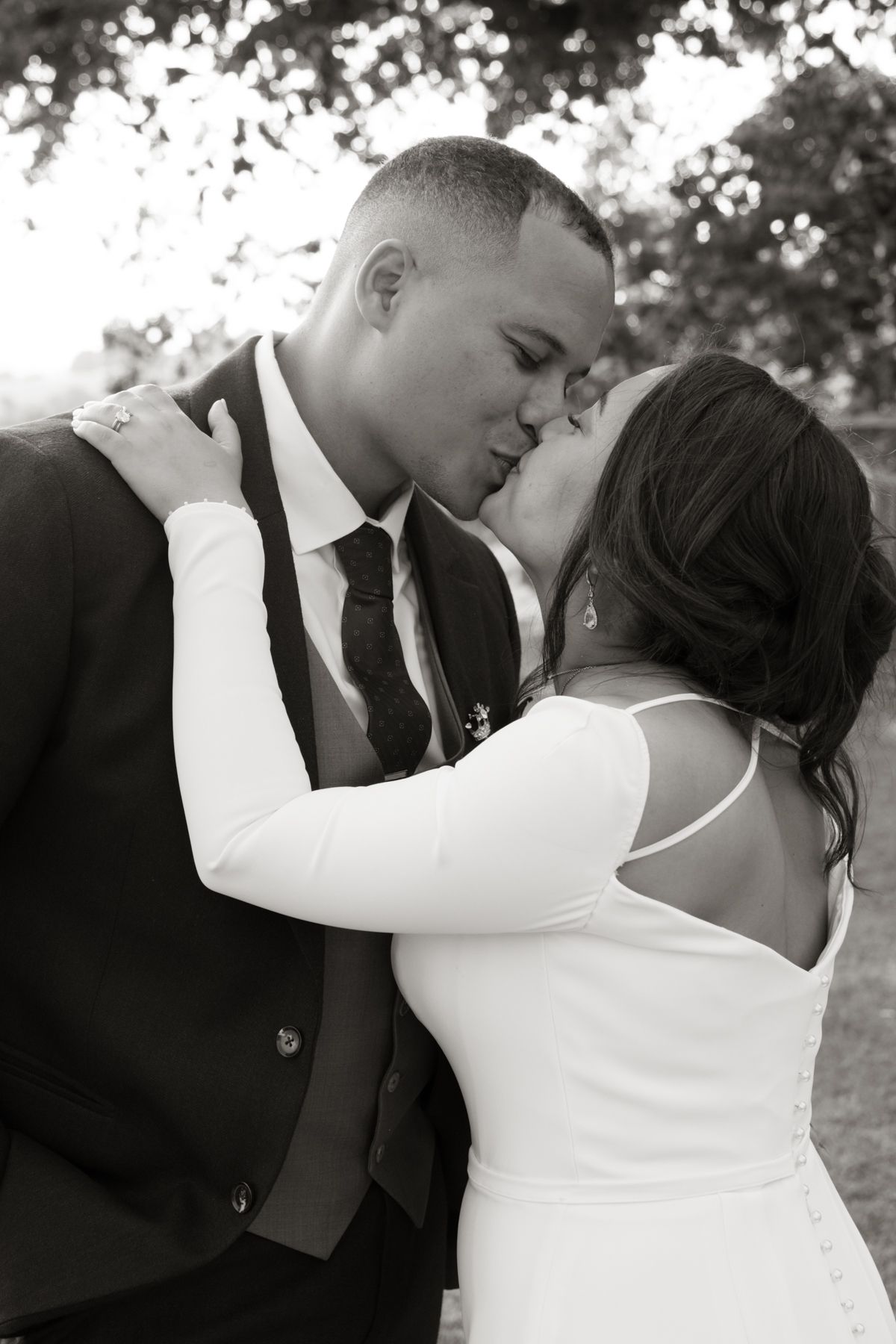 Black and white romantic photo of bride and groom sharing a kiss outdoors at their wedding.