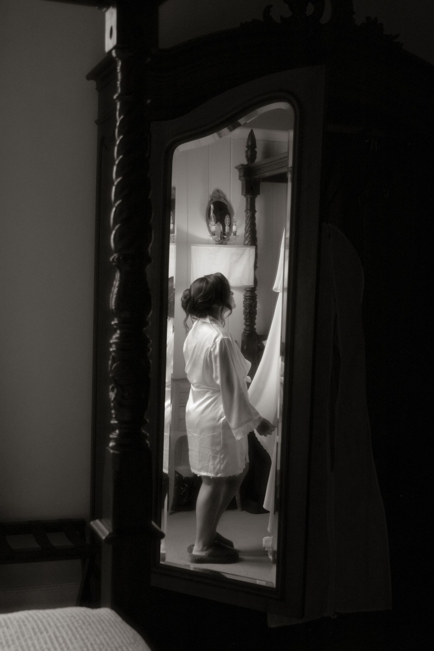 Bride in white robe reflected in ornate mirror while preparing for wedding ceremony.