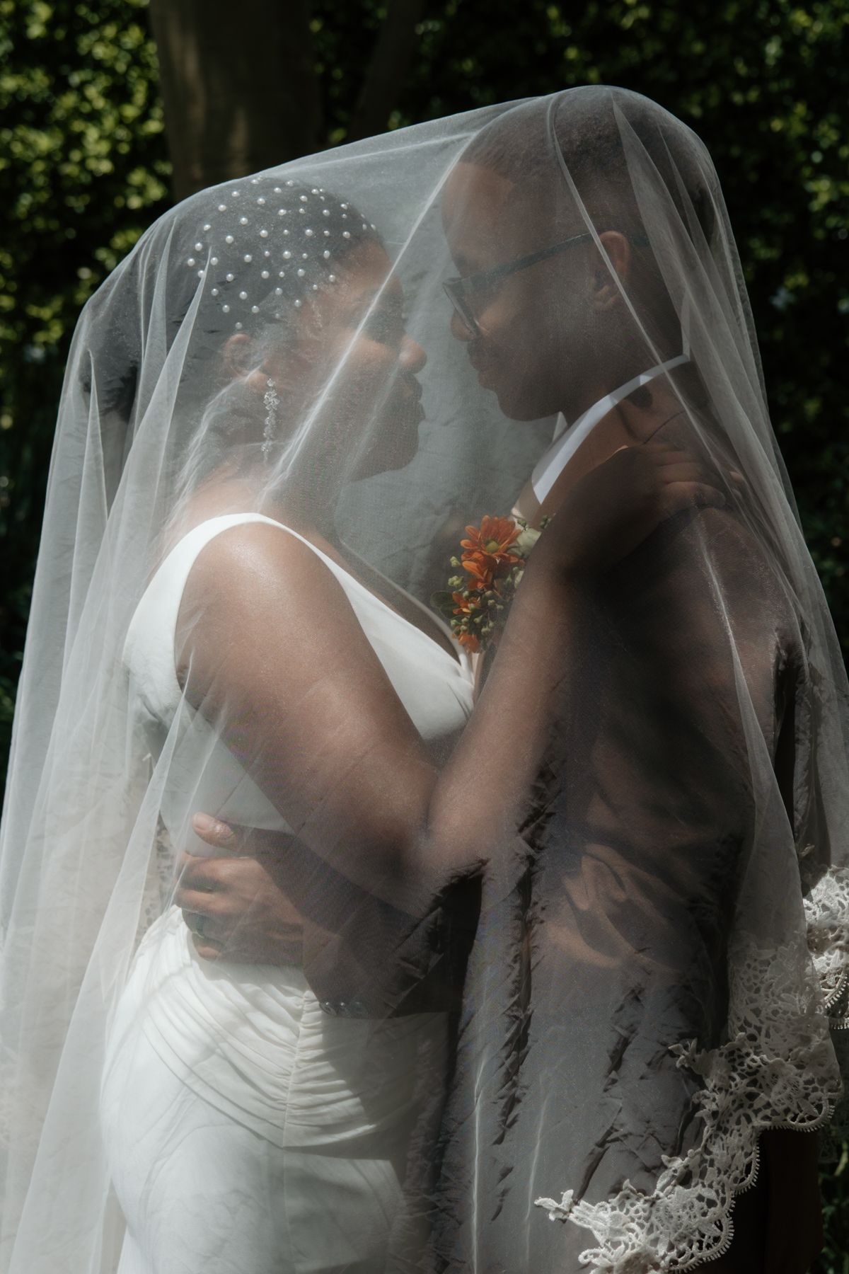 Bride and groom share an intimate moment beneath a lace-trimmed veil, faces close in a romantic embrace.