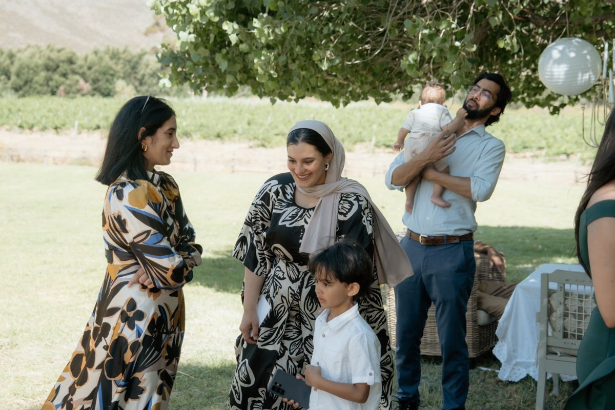 Wedding guests mingling outdoors on green lawn with mountains visible in the background.