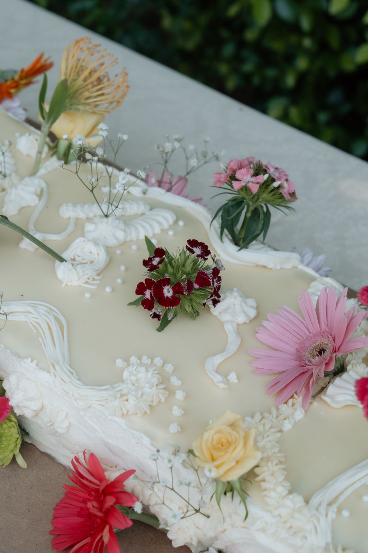 Elegant wedding cake decorated with colorful fresh flowers including pink gerberas, roses, and red carnations.