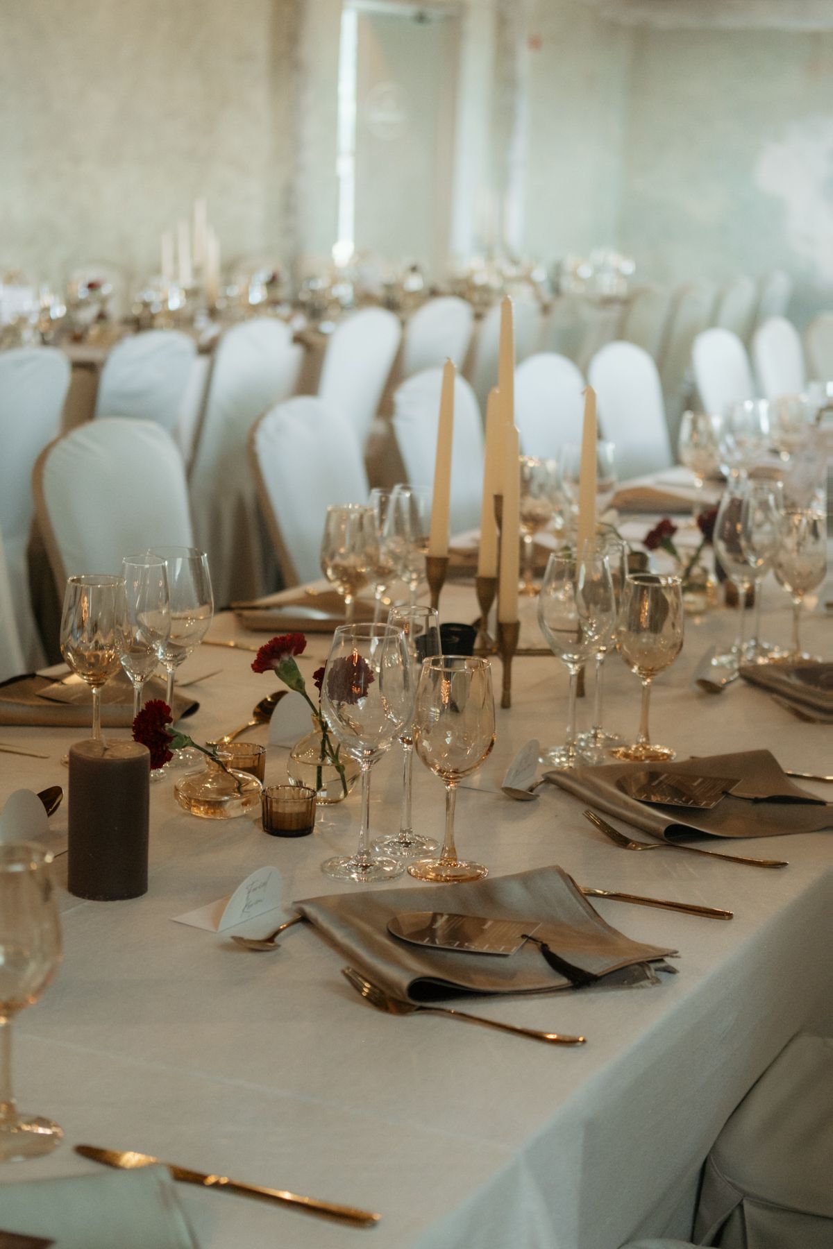 Elegant wedding reception table set with crystal glasses, tapered candles, and red floral accents.