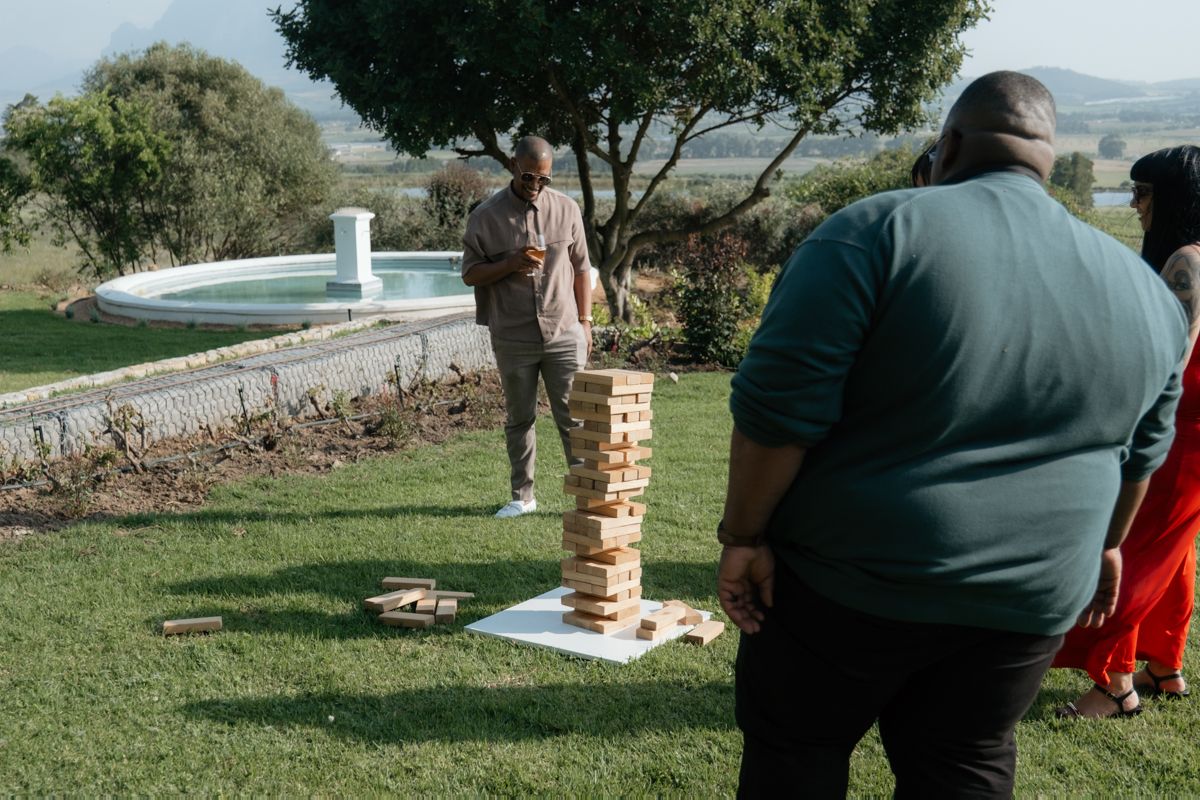 Wedding guests playing giant Jenga lawn game outdoors near pool at South African wine estate.