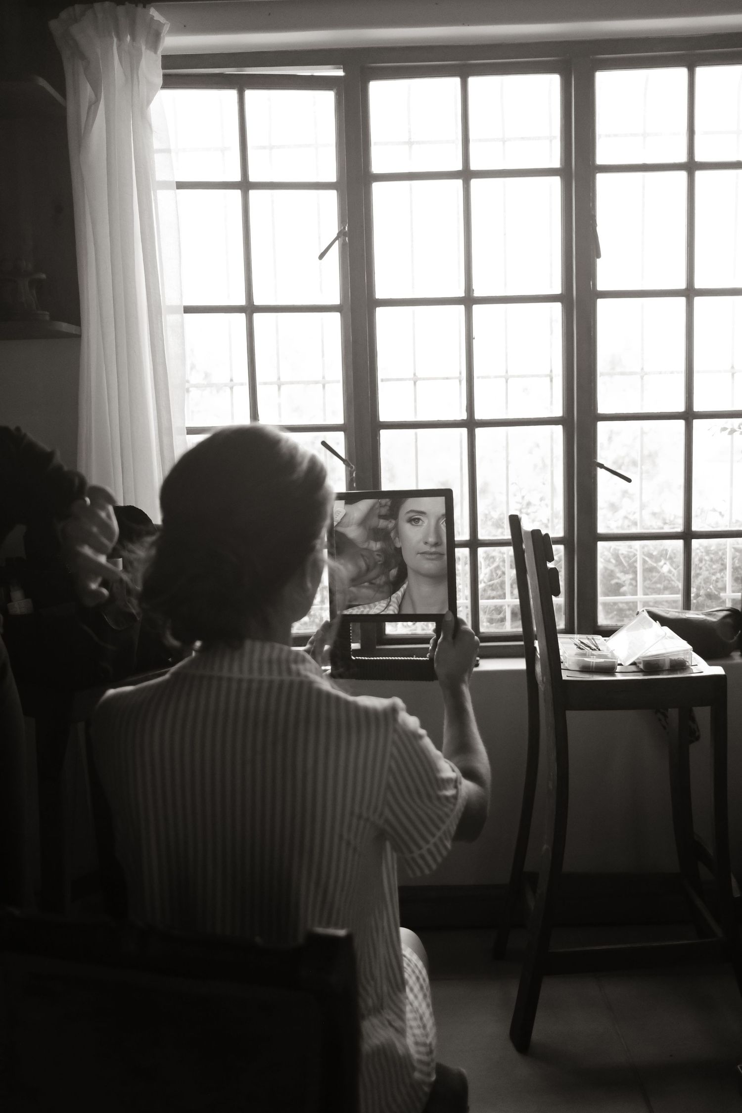Bride sits at vanity mirror getting ready for wedding in black and white photo.