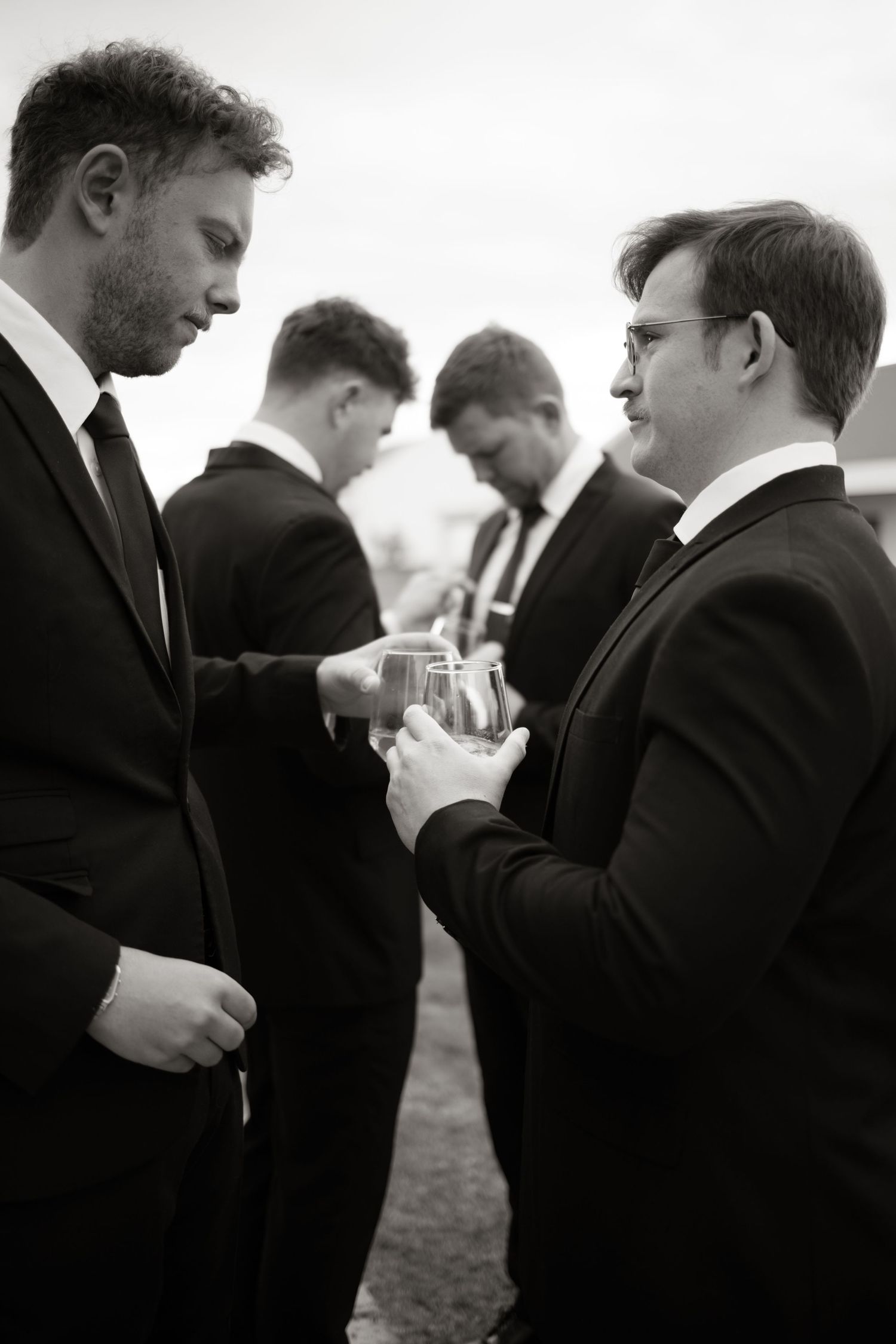 Group of formally dressed people in black and white having drinks and conversations at an outdoor gathering.