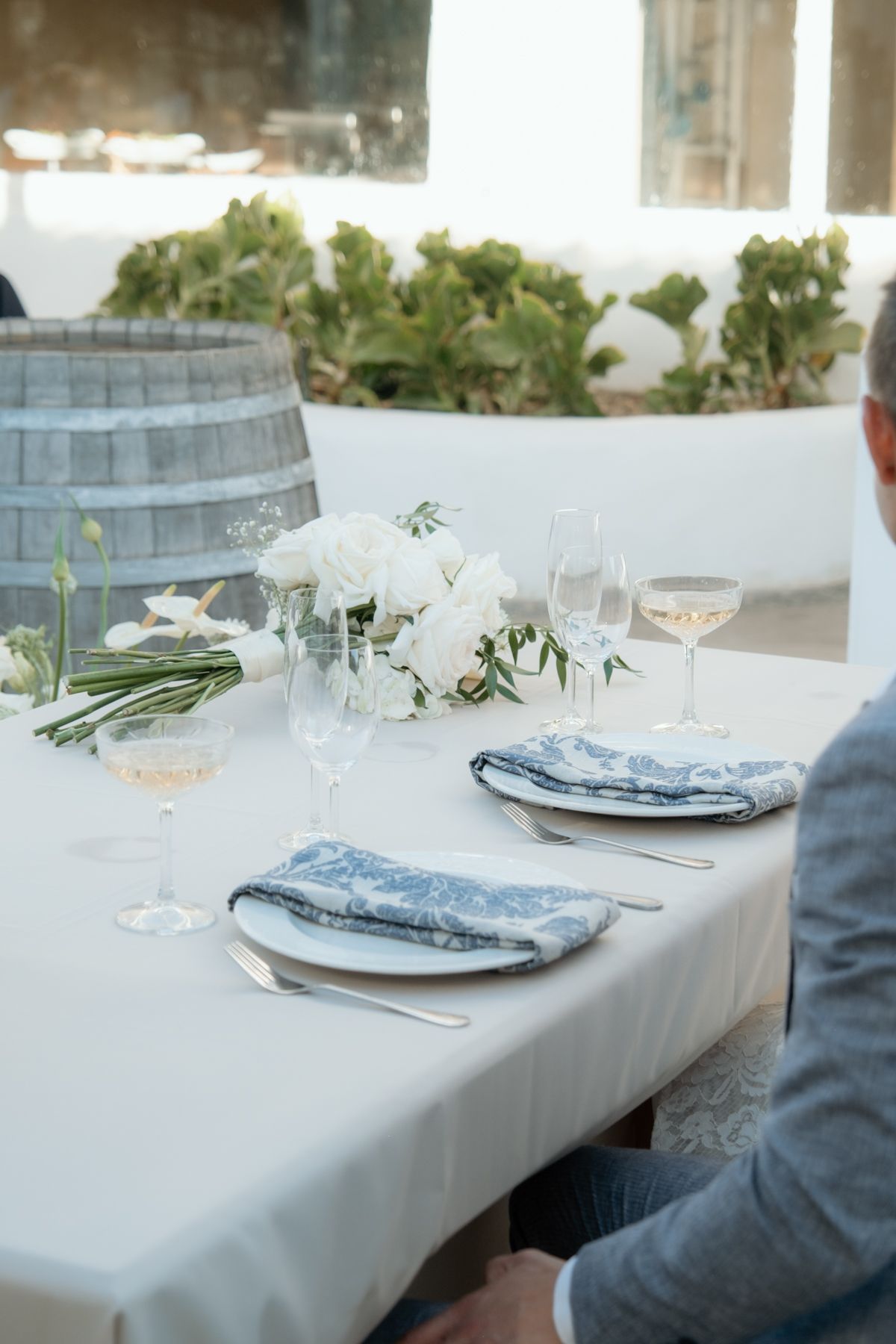 Elegant wedding reception table set with white florals, blue patterned napkins, and crystal glassware outdoors.