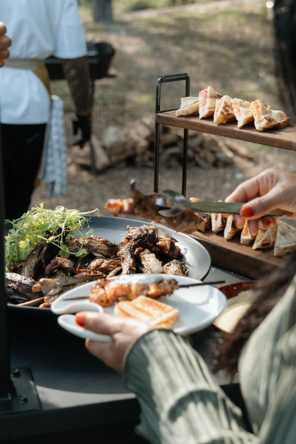 Close-up of hands serving grilled meats and appetizers at an elegant outdoor wedding catering station.