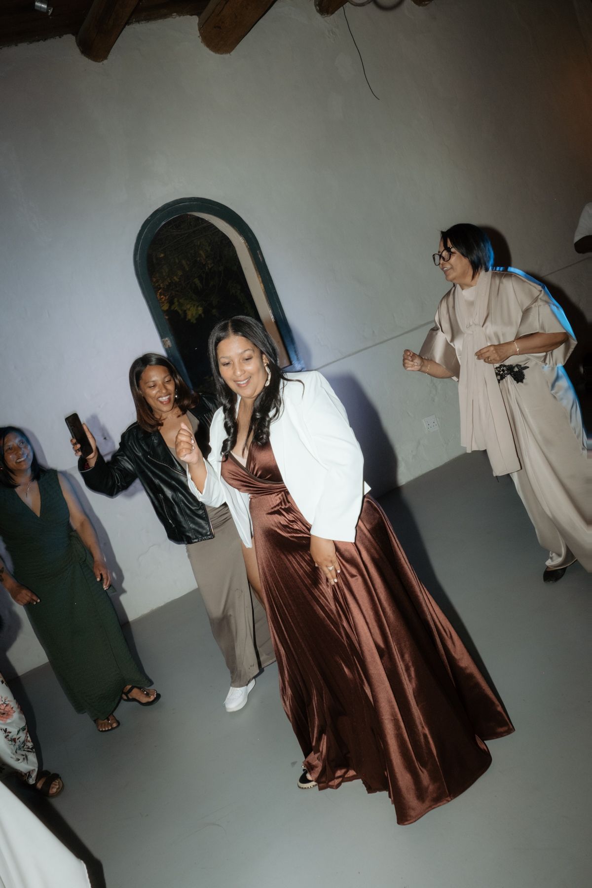 Woman in brown satin skirt dancing joyfully with guests at a lively wedding reception.