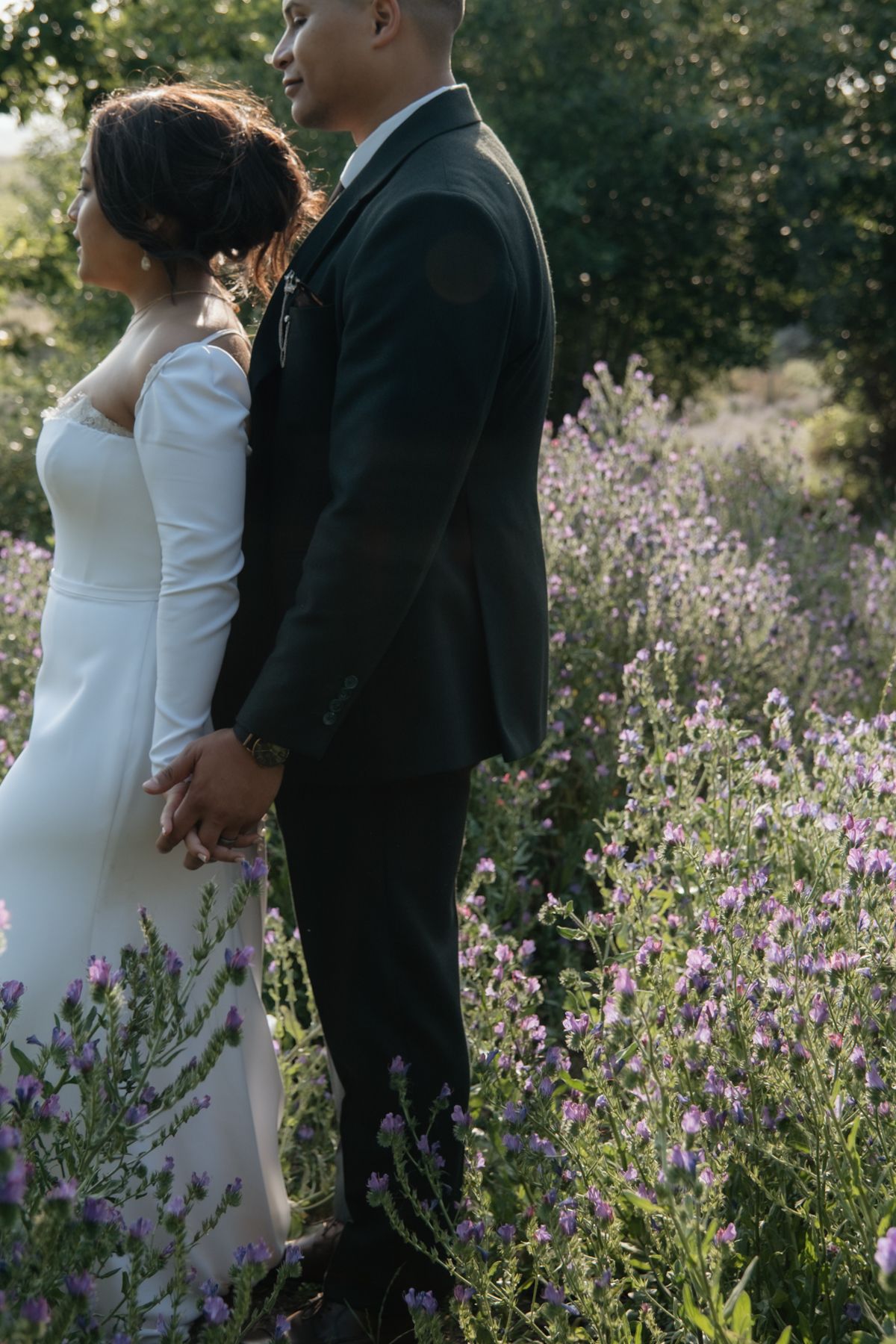 Bride and groom holding hands while standing together in a blooming lavender field.