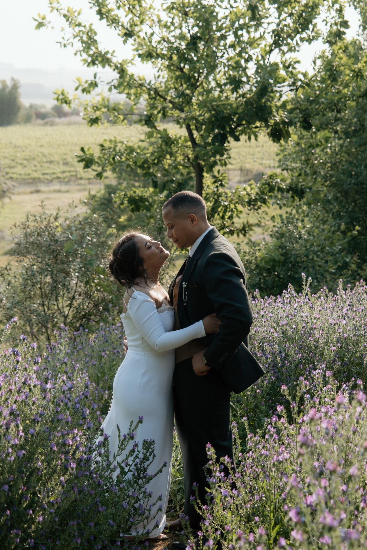 Bride and groom share a romantic kiss in a lavender field surrounded by lush greenery.