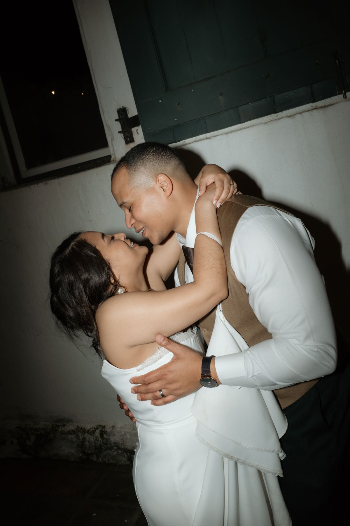 Bride and groom share a romantic intimate embrace and kiss during their wedding reception at night.