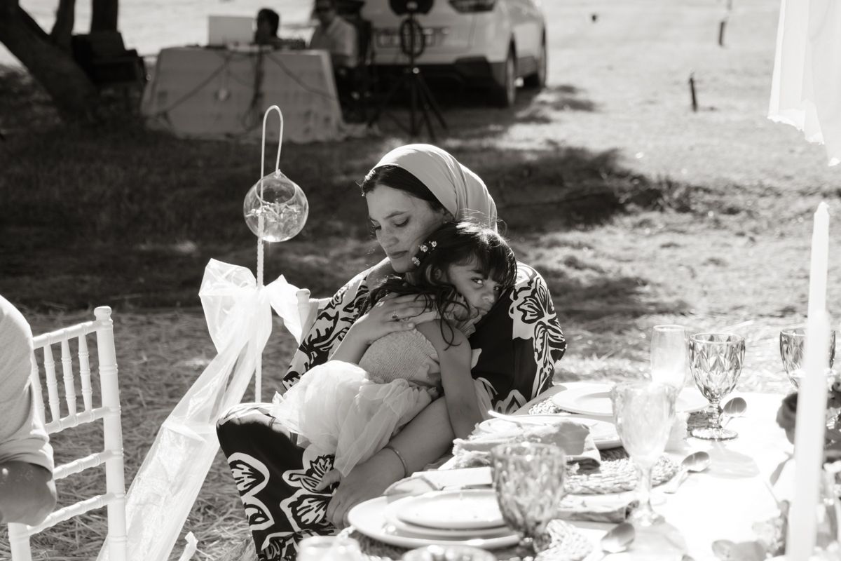 Black and white photo of bride embracing a child at outdoor wedding reception table.