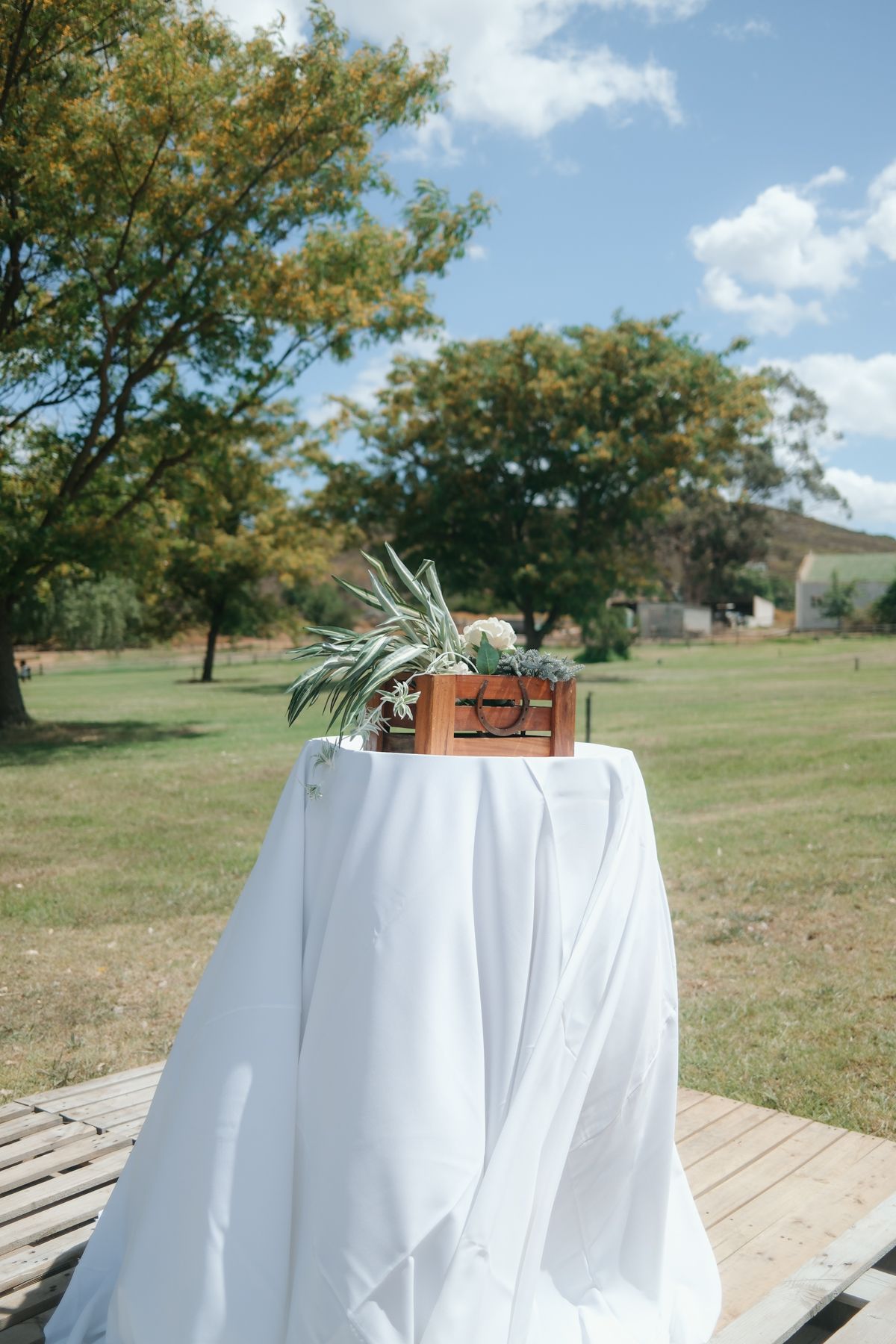 Elegant outdoor wedding altar table with white linen and succulent centerpiece on wooden platform in green park.