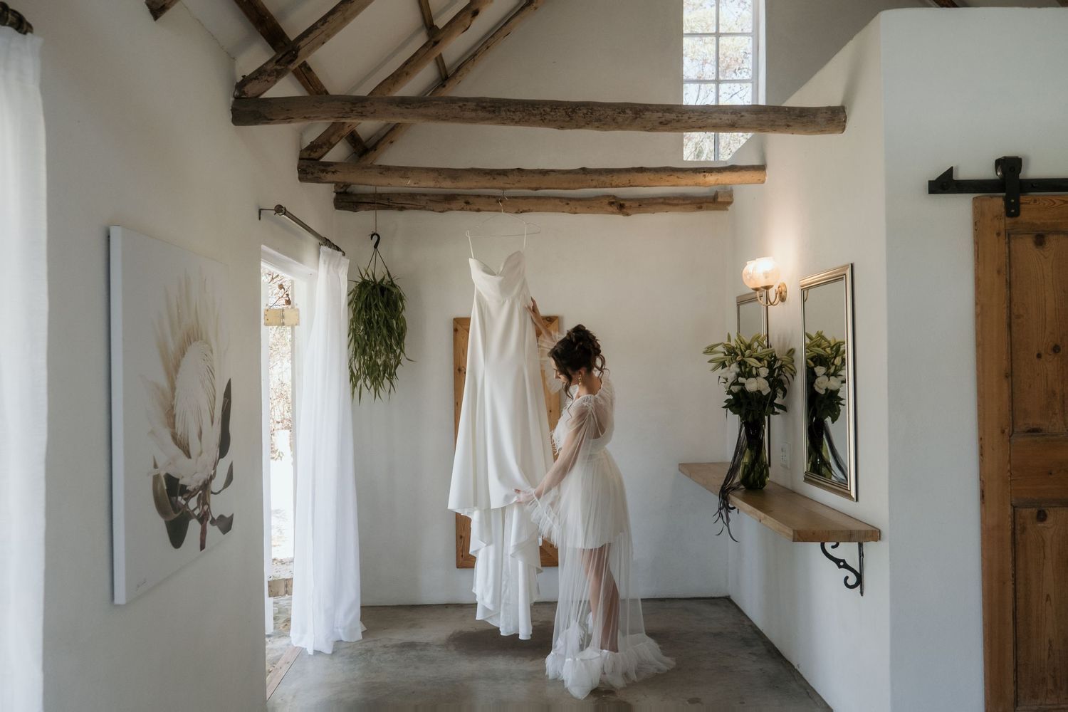 Elegant white wedding dress displayed in a rustic room of Murasie Wedding Venue with wooden beams and natural light.