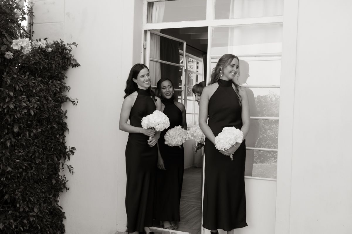 Three bridesmaids in black halter dresses holding white bouquets at wedding.