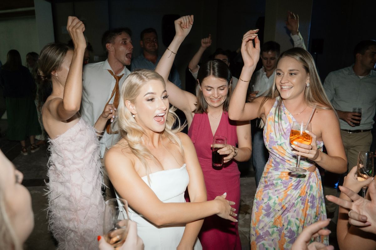 Bride in white dress dancing joyfully with guests in colorful outfits on the wedding reception dance floor.