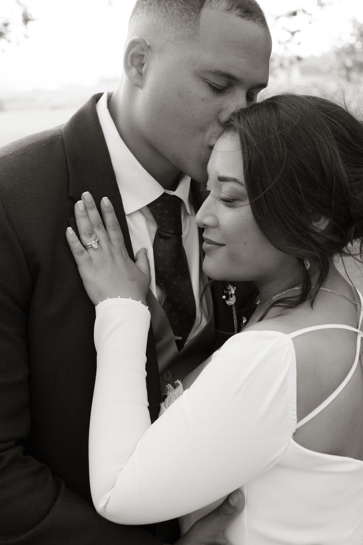 Black and white portrait of groom kissing bride on forehead as she places hand on his chest.