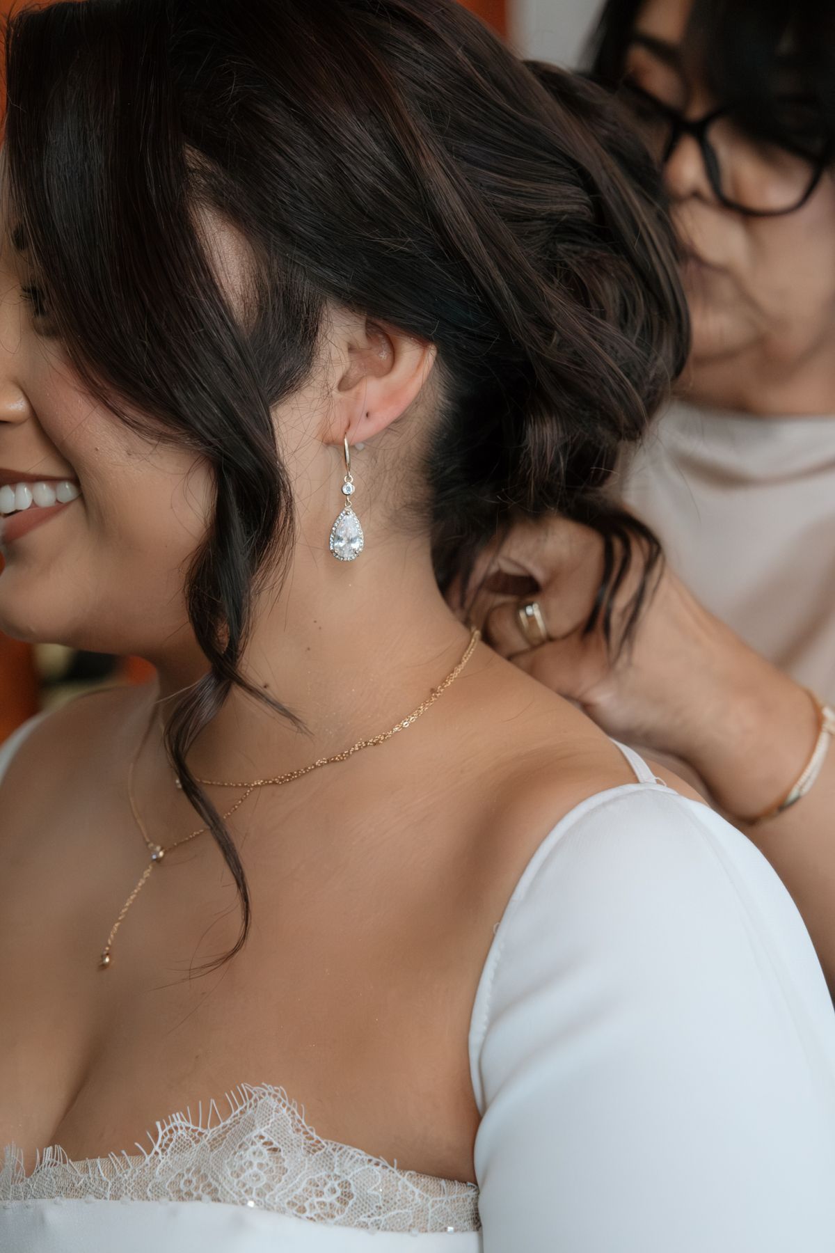 Close-up of bride's elegant updo with teardrop crystal earring and delicate gold necklace on wedding day.