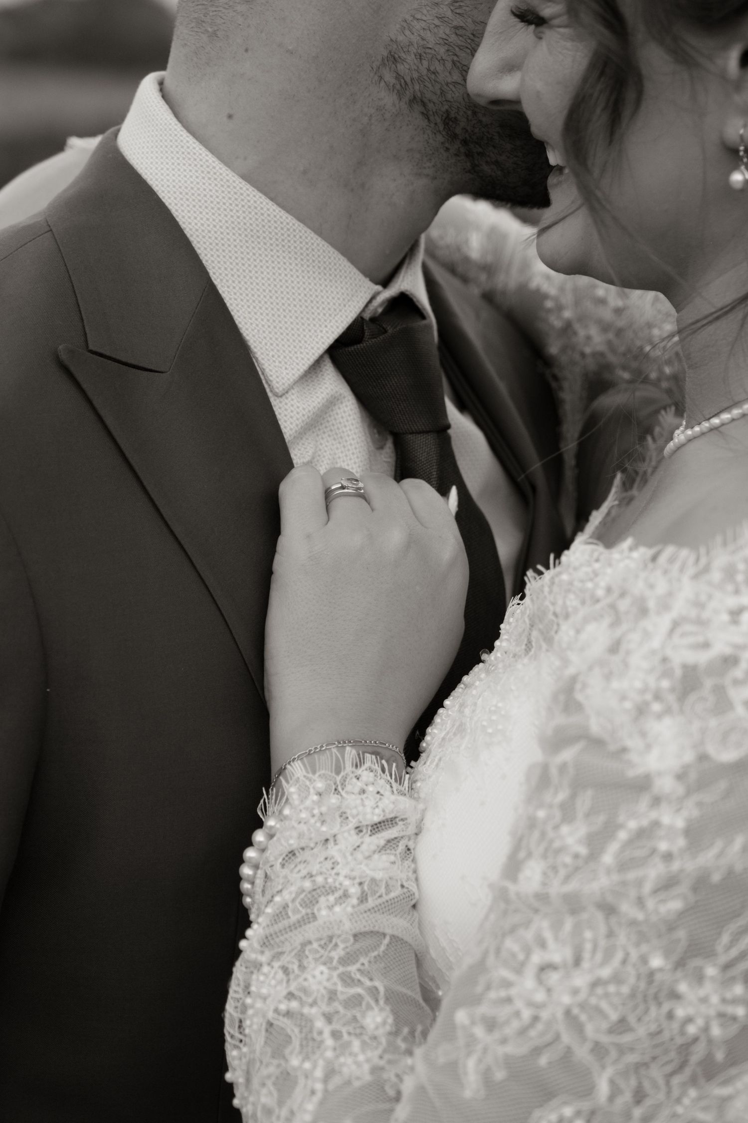 Black and white photo of bride in lace gown adjusting grooms tie at wedding ceremony.
