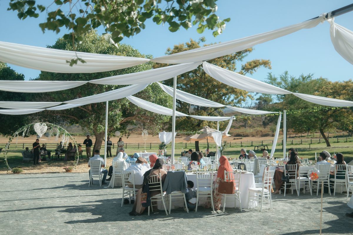 Elegant outdoor wedding reception with white draped canopy over round tables in sunny venue.