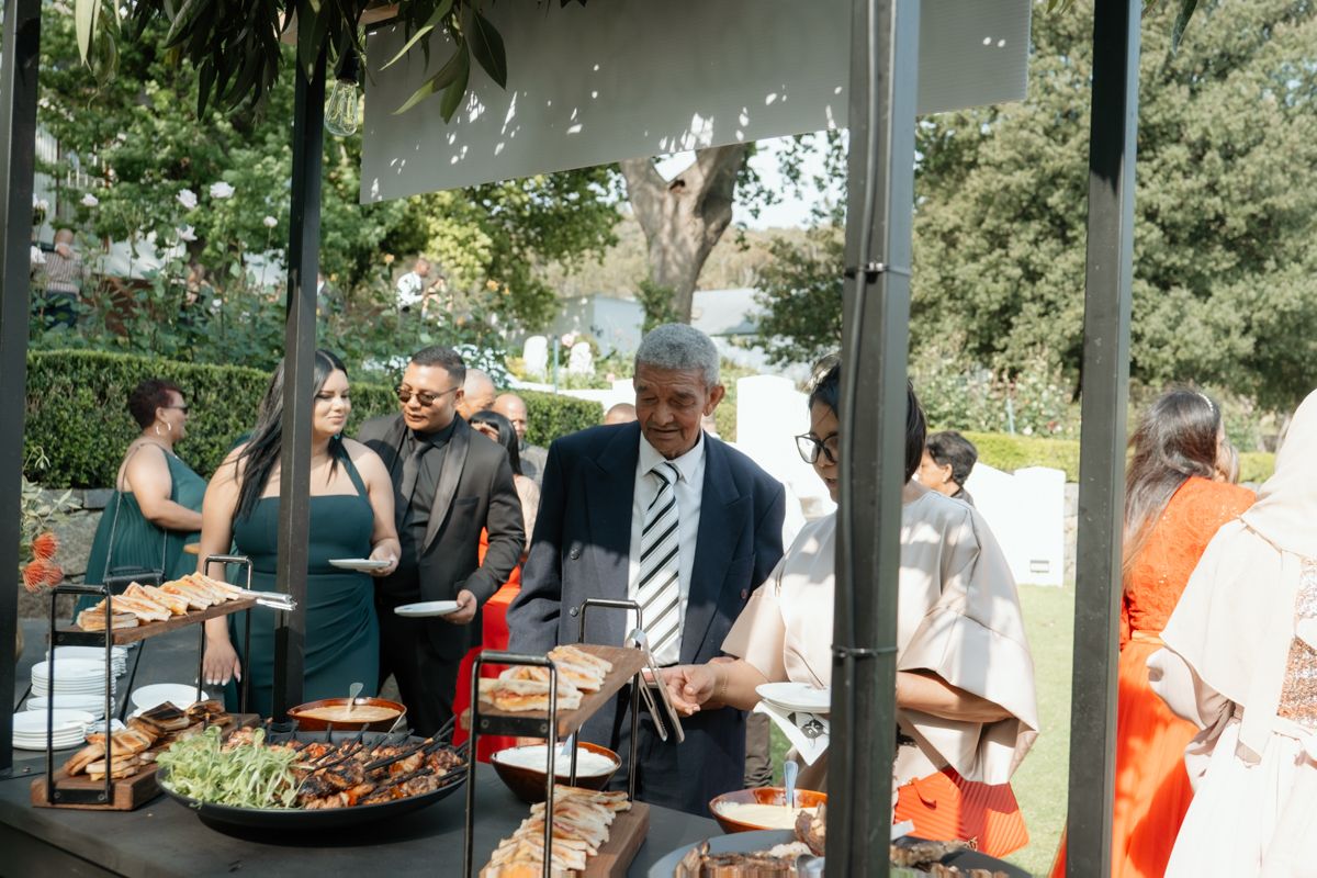 Wedding guests in formal attire serving themselves at an outdoor catered food station.