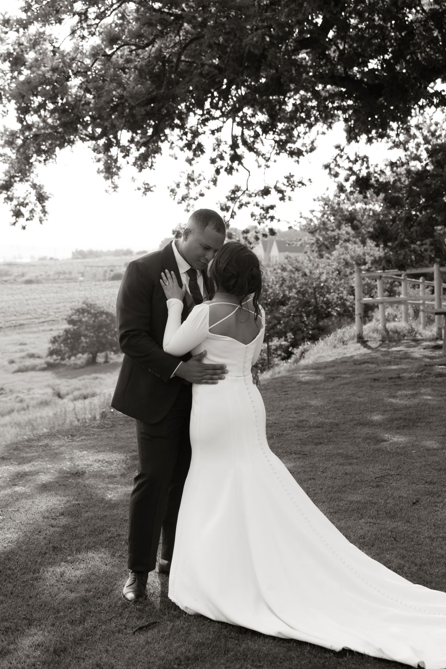 Black and white photo of bride and groom sharing a romantic kiss under a tree outdoors.