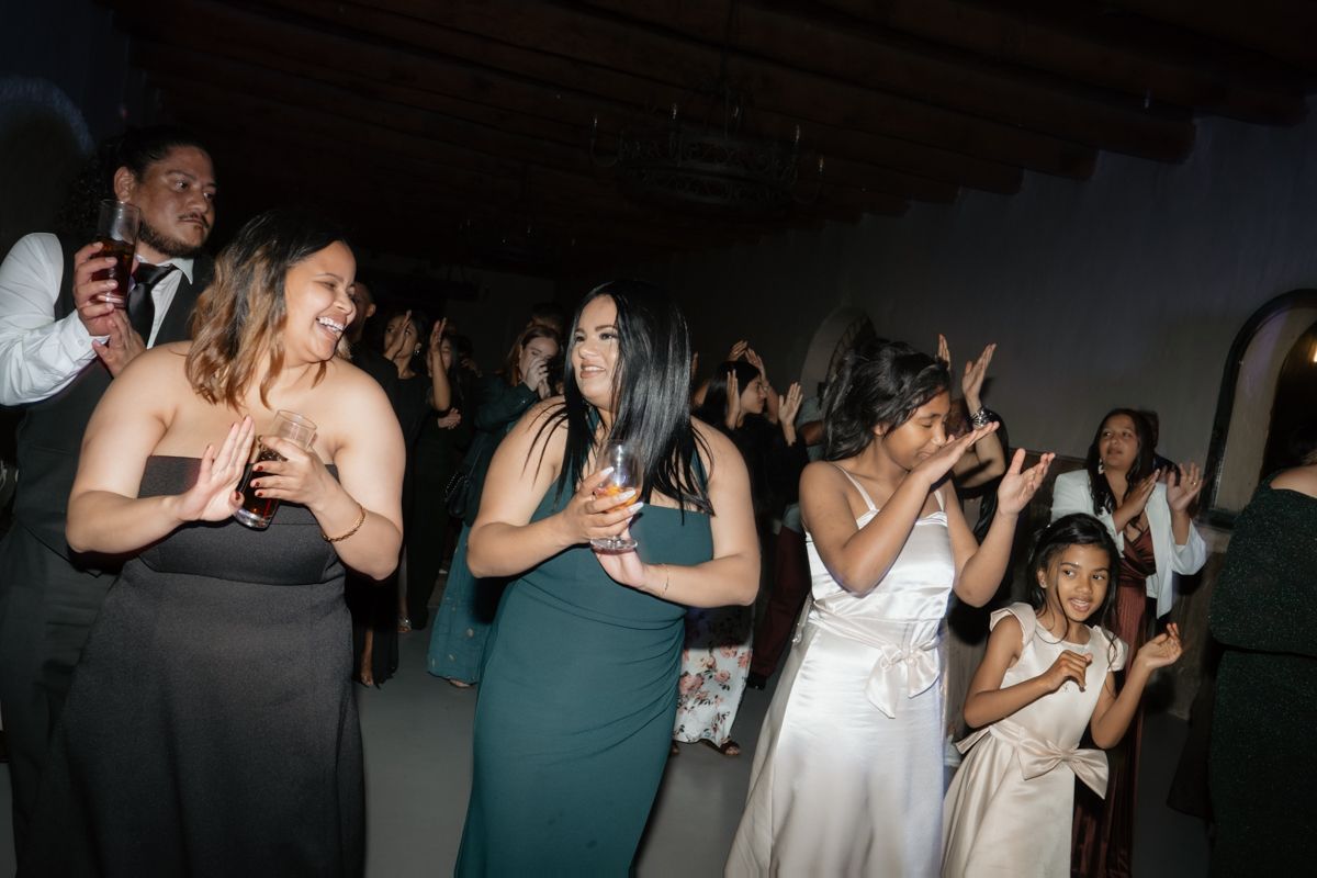 Wedding guests in formal attire dancing and celebrating joyfully on the dance floor at a reception.