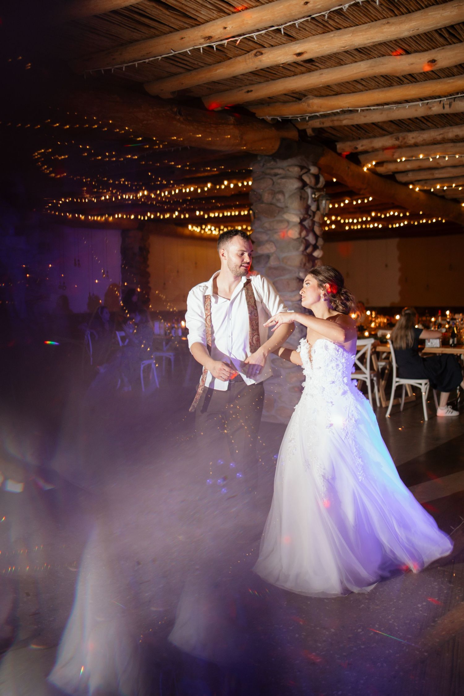 Bride and groom share first dance in elegant rustic venue adorned with twinkling string lights.