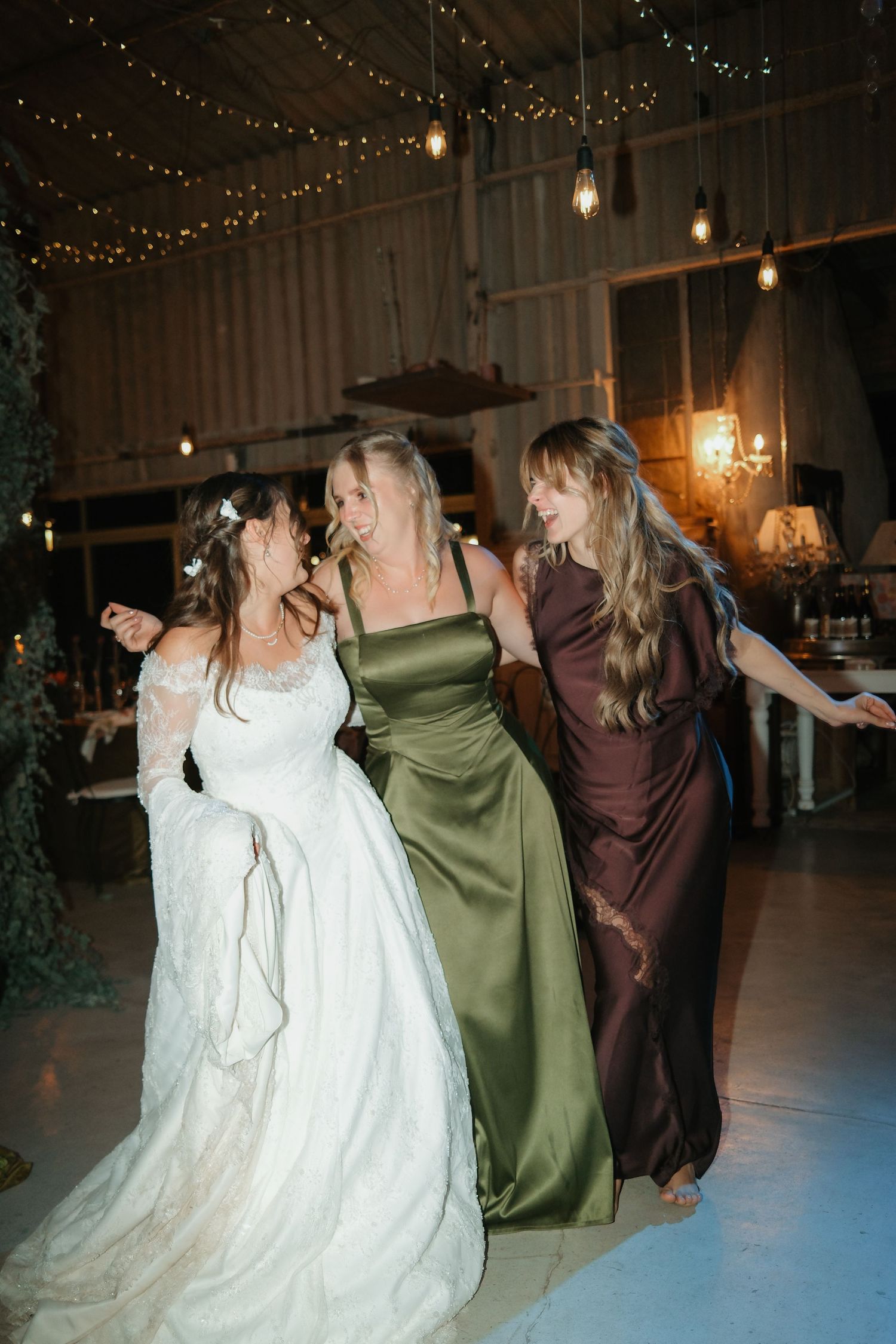 Bride dancing joyfully with bridesmaids in green and brown gowns at wedding reception.