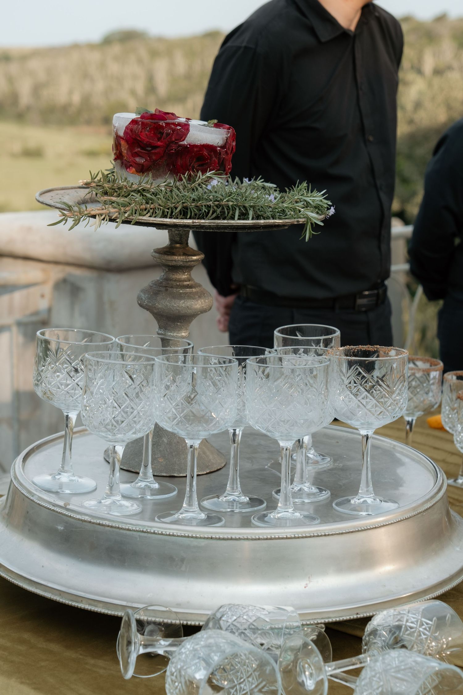 Crystal champagne coupes arranged on silver tray with red roses and rosemary at wedding reception.