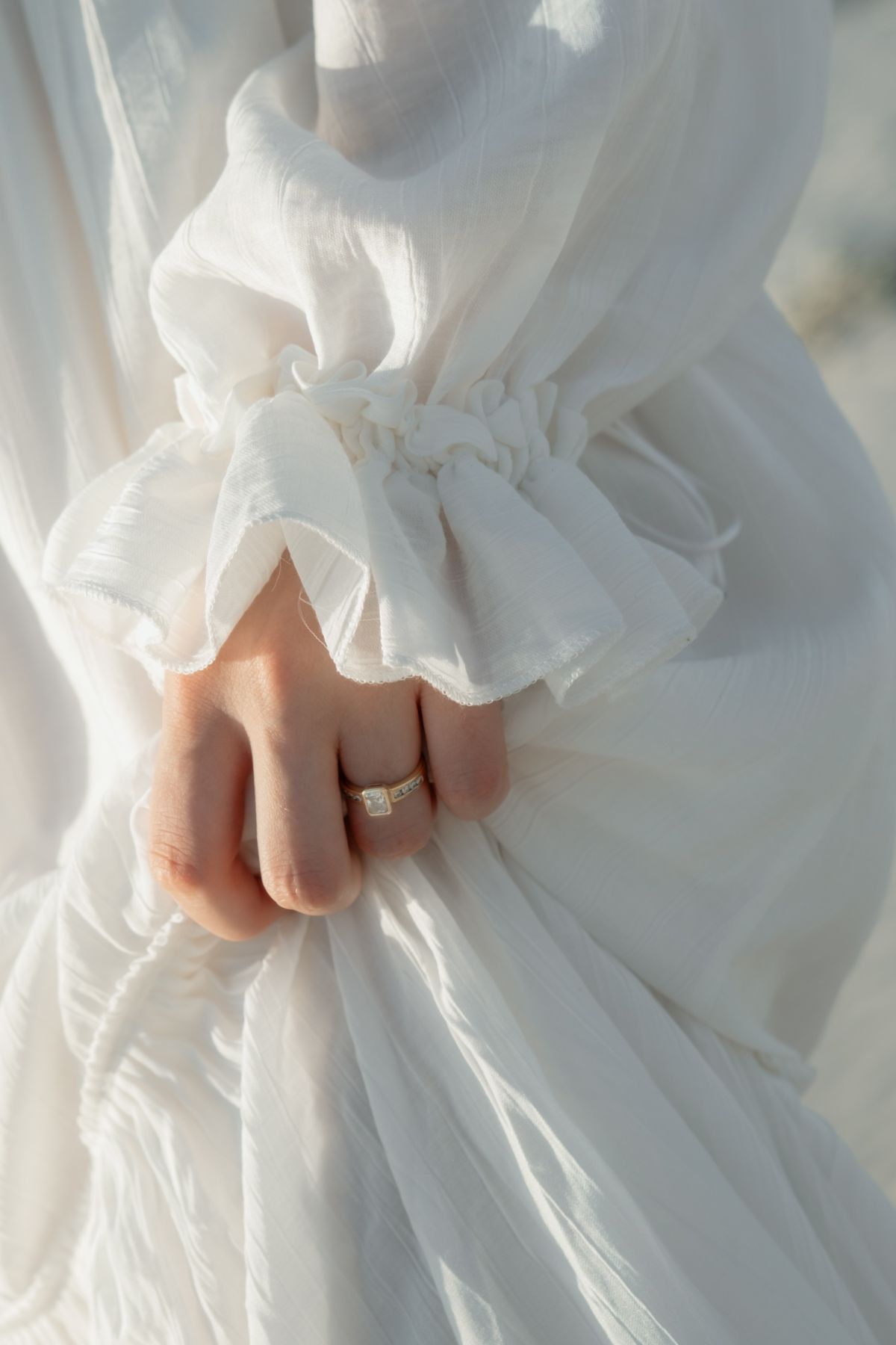 Close-up details of a white wedding dress with delicate fabric folds and a wedding ring visible on a hand.