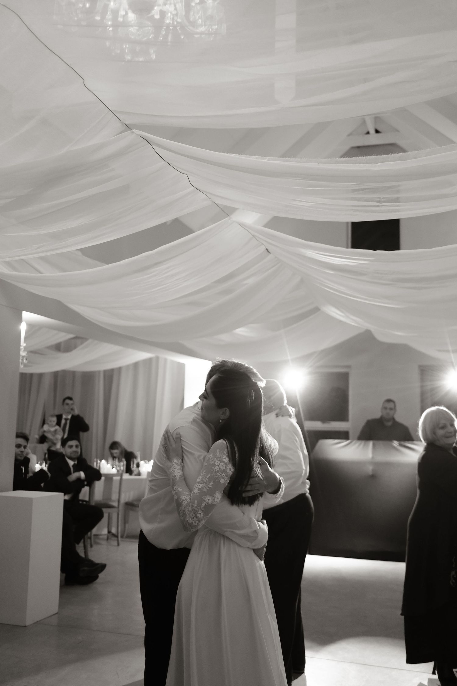 Black and white photo of newlyweds sharing their first dance under draped white fabric ceiling decor.