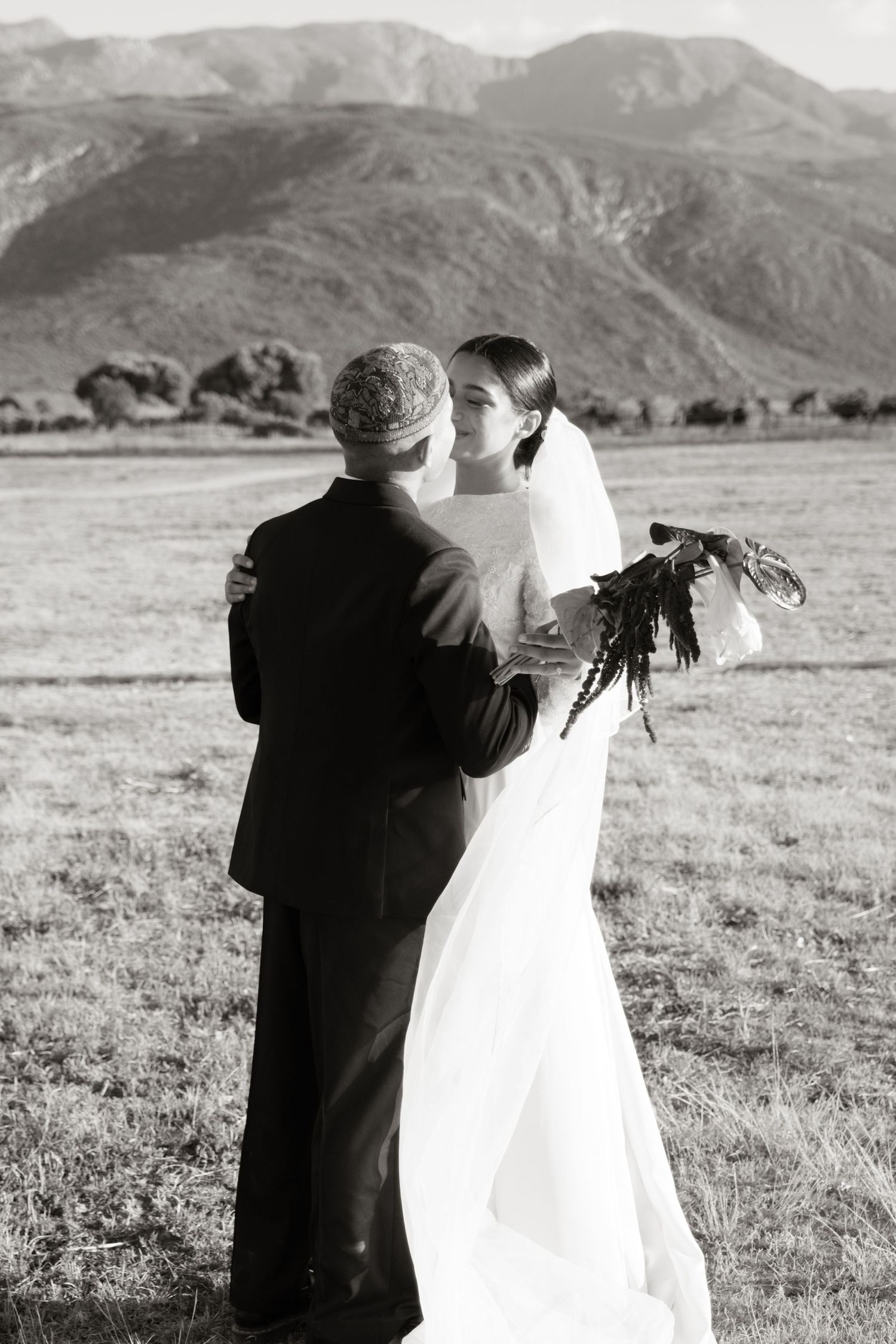 Black and white photo of bride and groom embracing in a scenic mountain landscape.