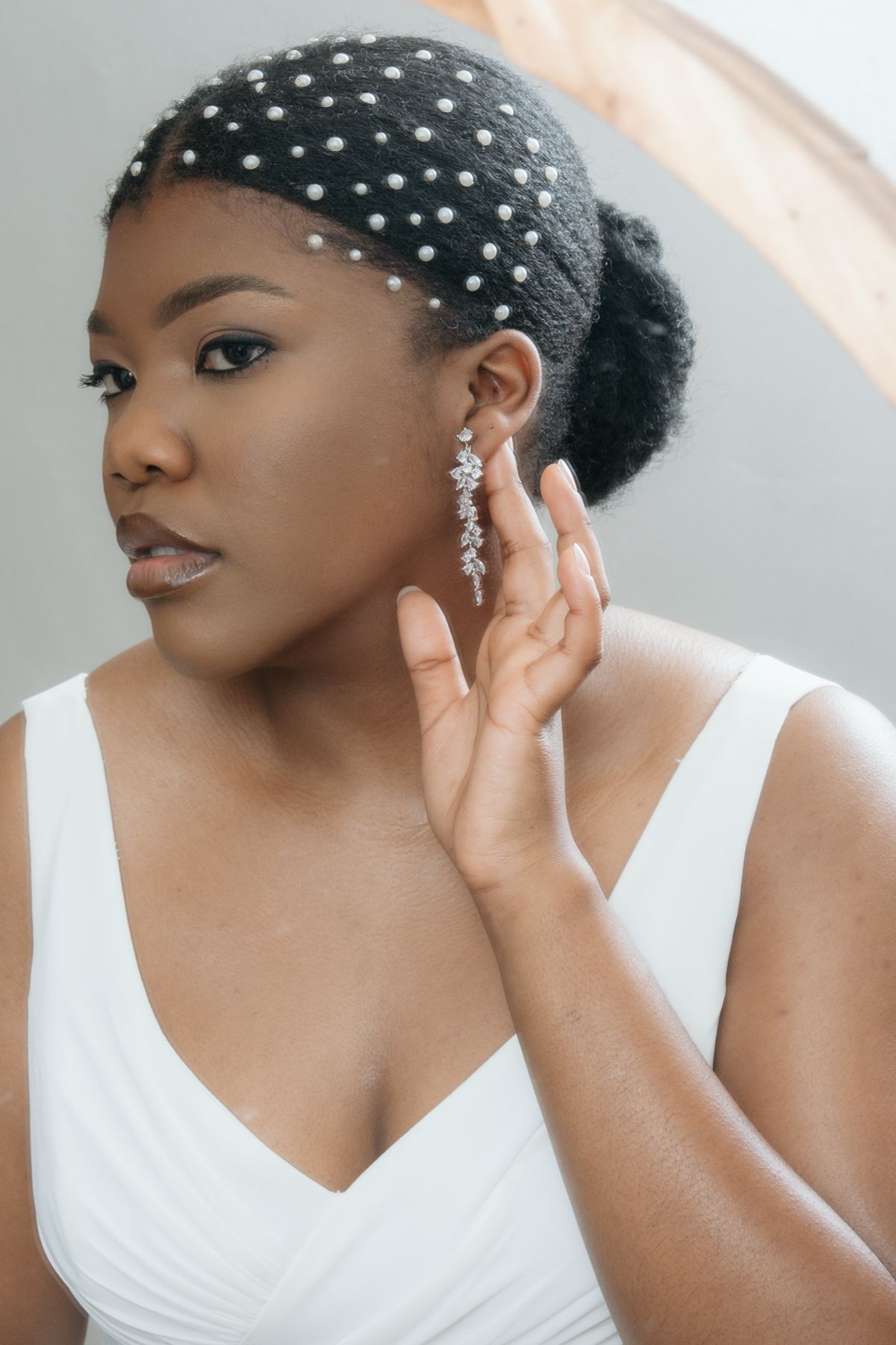 Bride wearing pearl hair accessories and crystal drop earrings in elegant updo with white bridal gown.