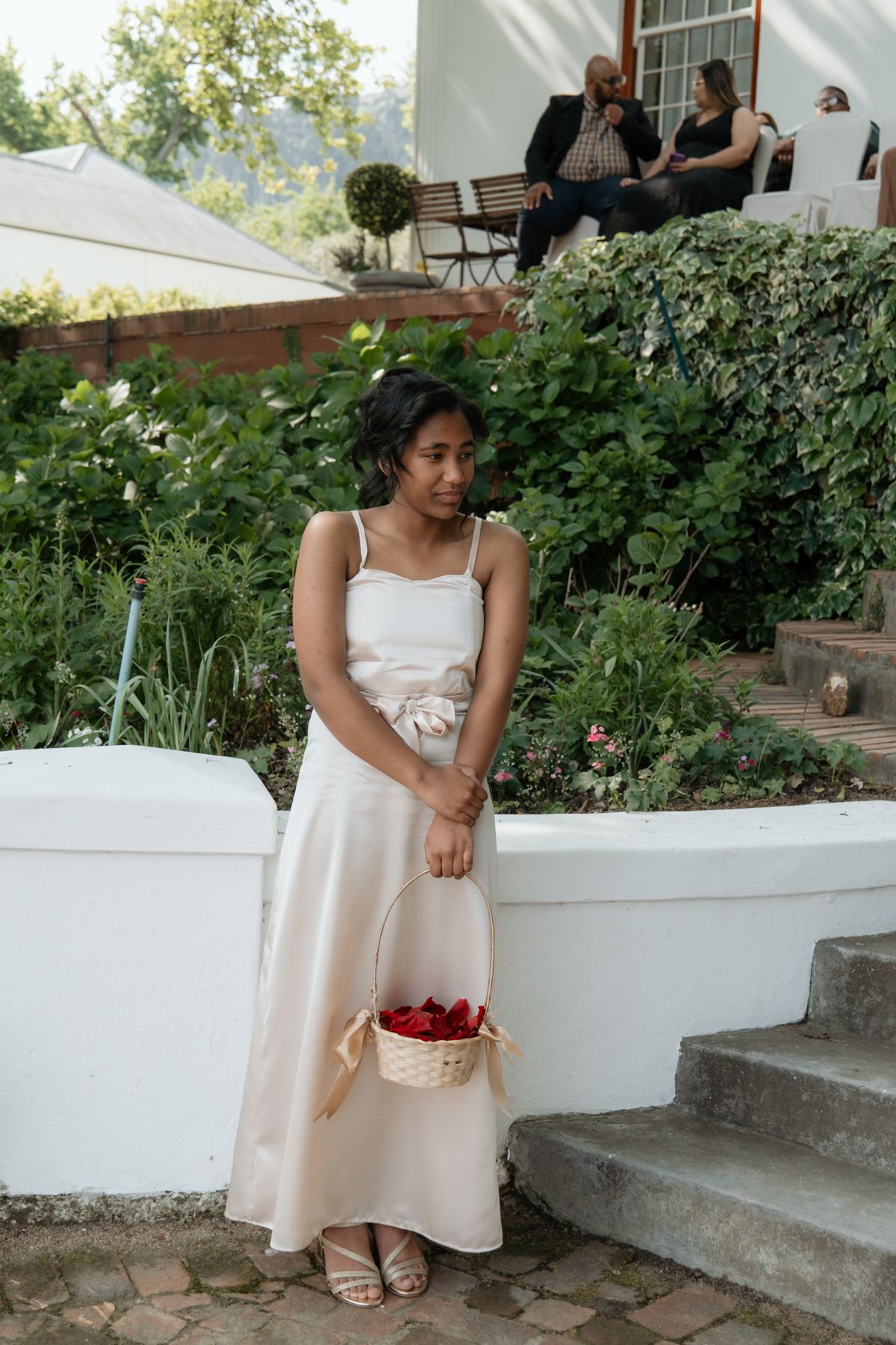 Young woman in white dress holding flower basket at wedding venue.