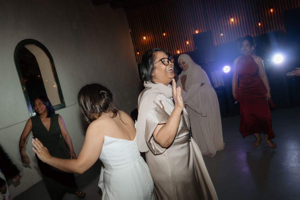 Guests dancing and celebrating with bride in white gown at festive indoor wedding reception party.