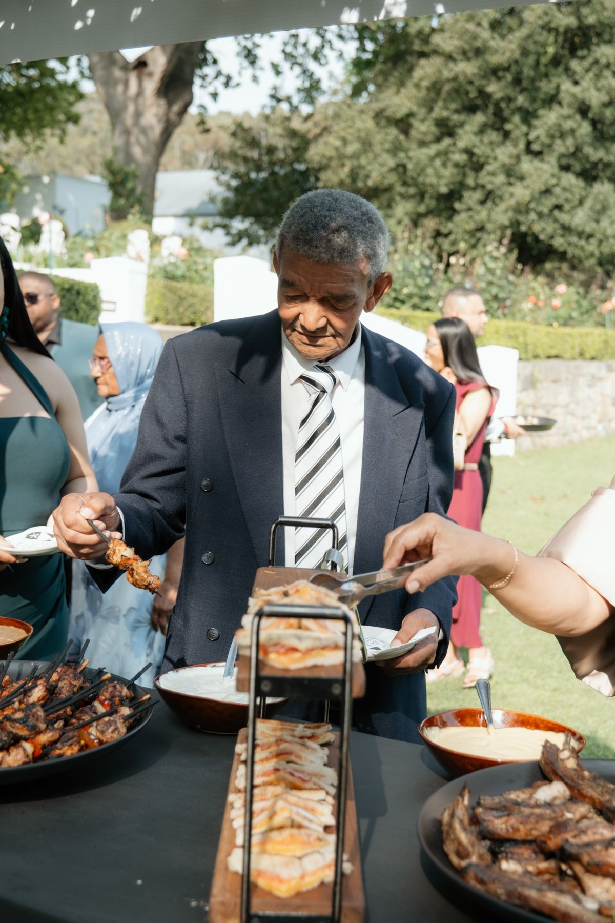 Wedding guest serving himself at outdoor braai buffet station during South African wedding reception.