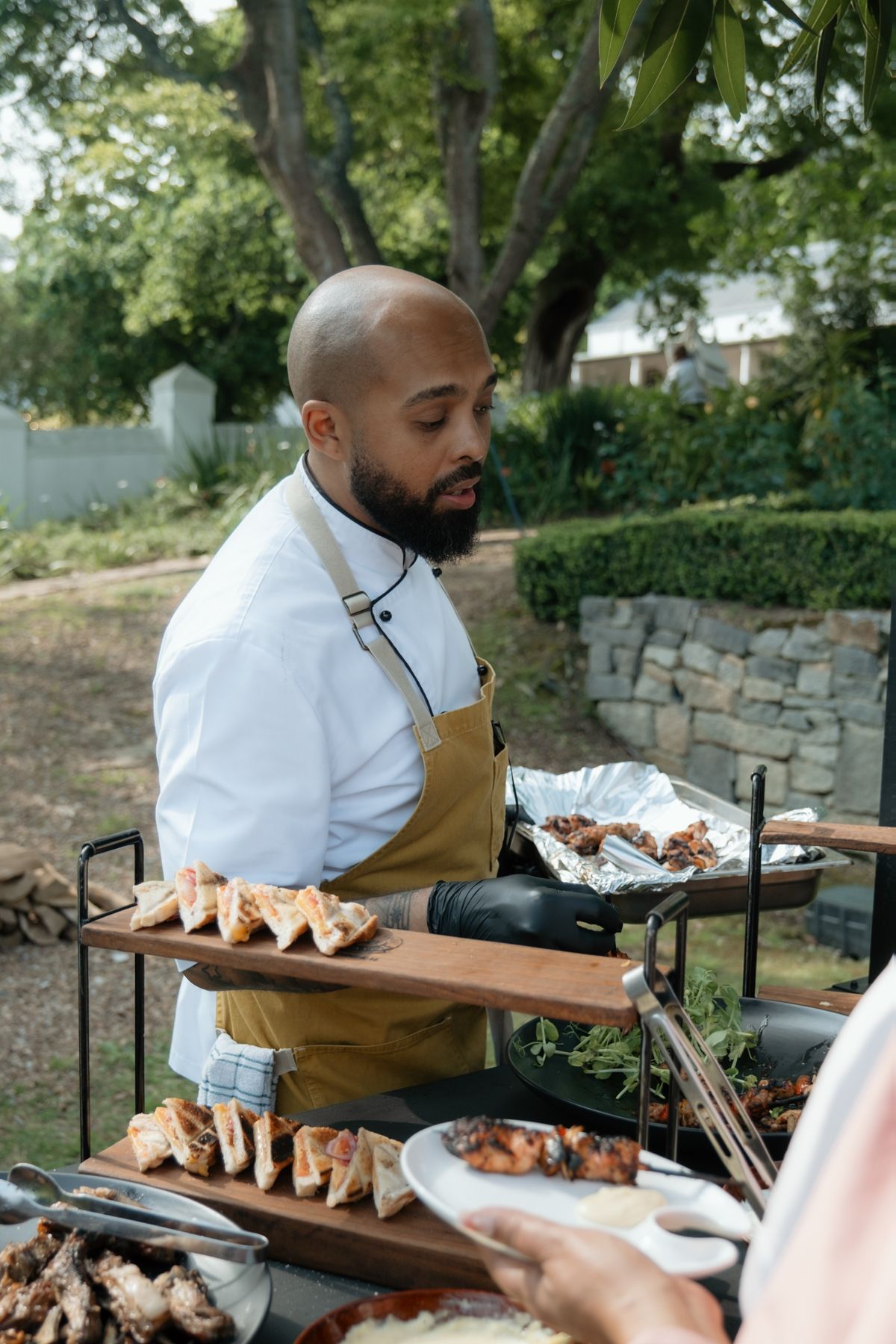 Chef in white uniform and yellow apron serving food at an elegant outdoor wedding reception.