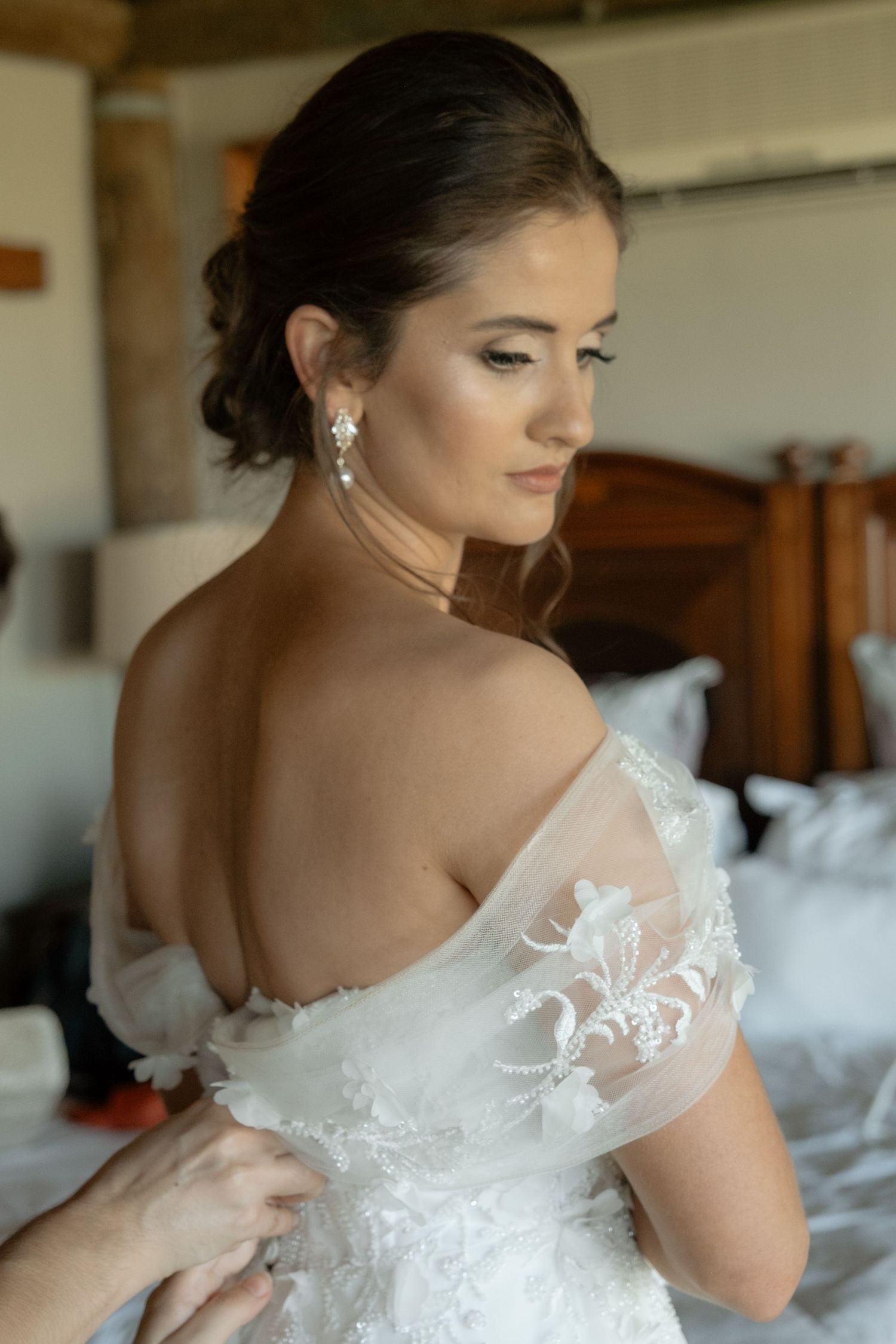 Bride in an off-shoulder lace wedding gown with elegant updo and crystal earrings on her wedding day.