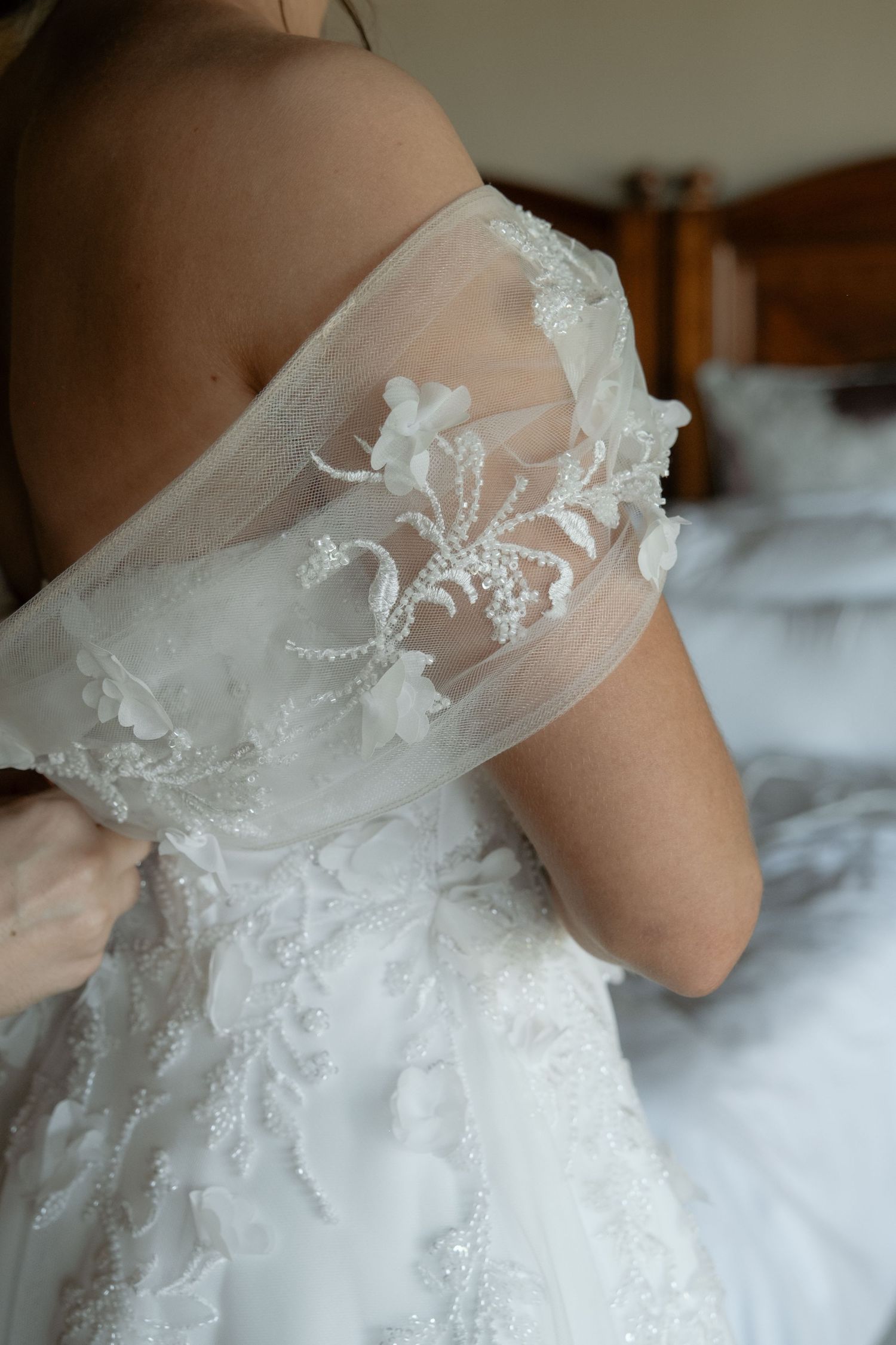 Close-up detail of off-shoulder wedding gown with delicate floral lace and pearl embroidery.