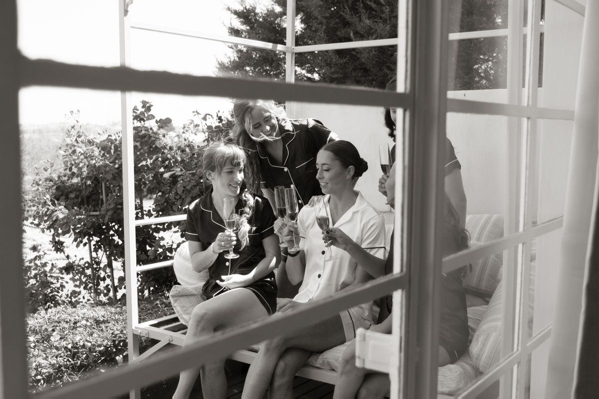 Black and white photo of two women sitting at a window sill enjoying champagne together.