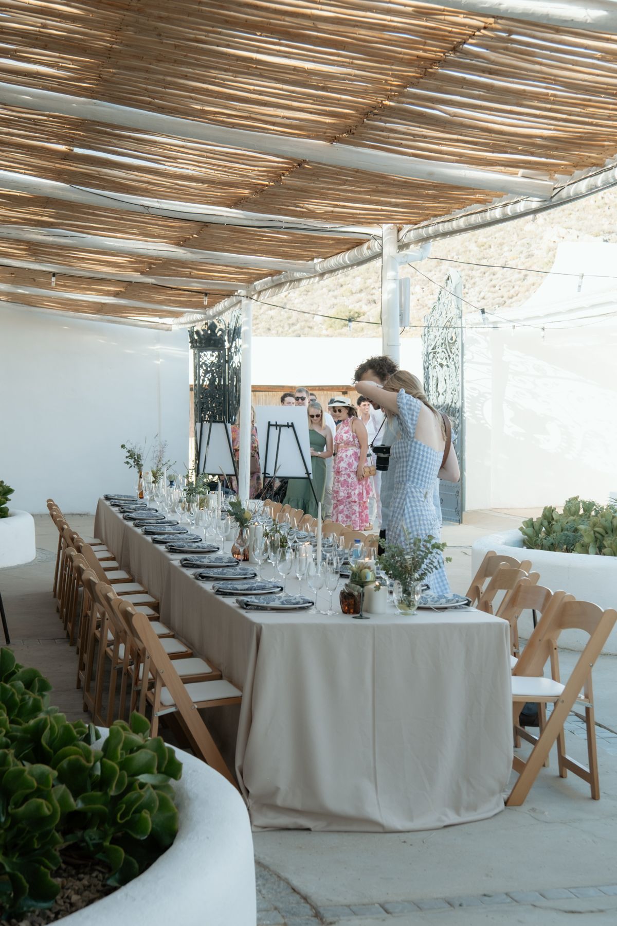 Elegant outdoor wedding reception table set under rustic reed canopy with floral centerpieces.