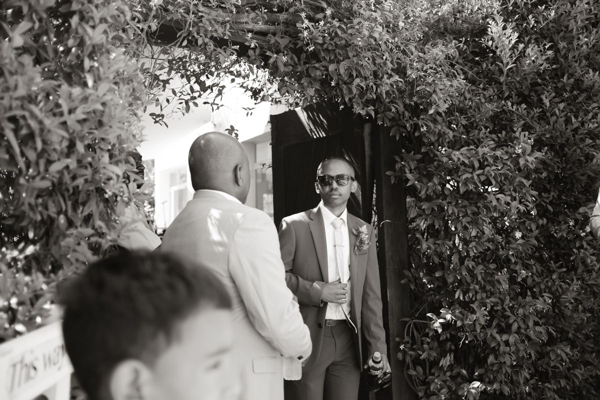 Black and white photo of two men in suits conversing outdoors under lush green archway.