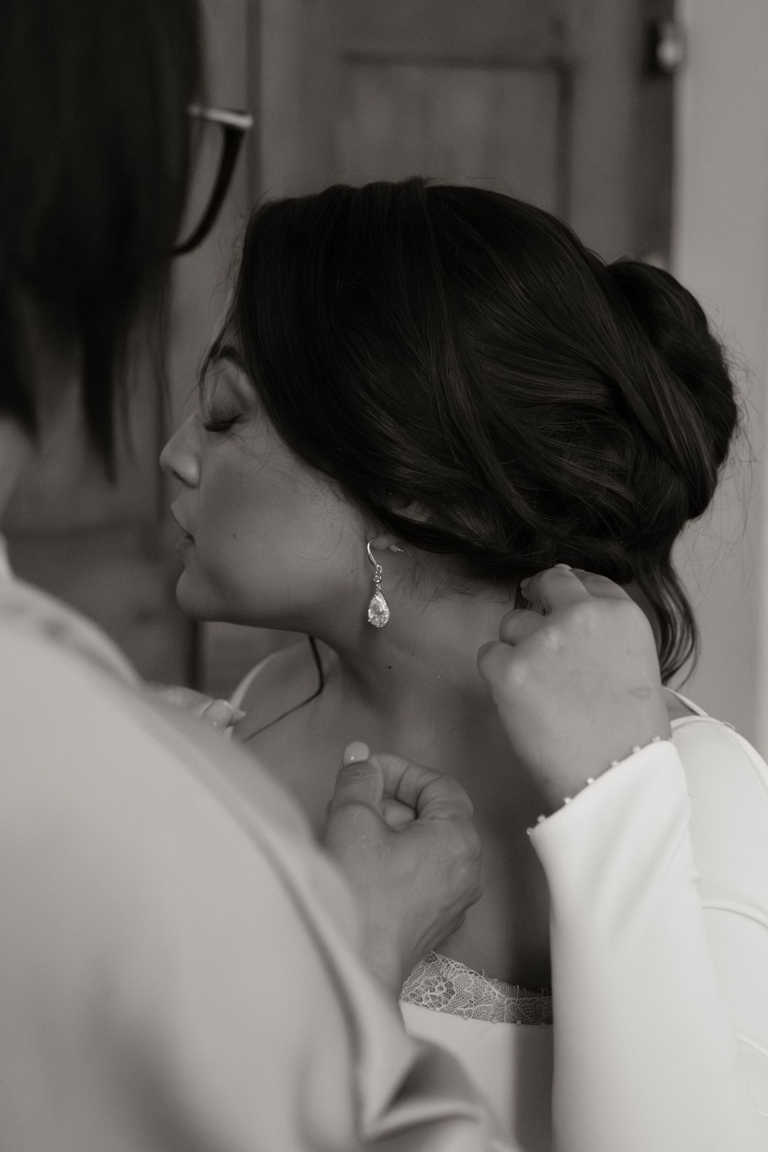 Black and white photo of bride having earring put on during wedding preparations.