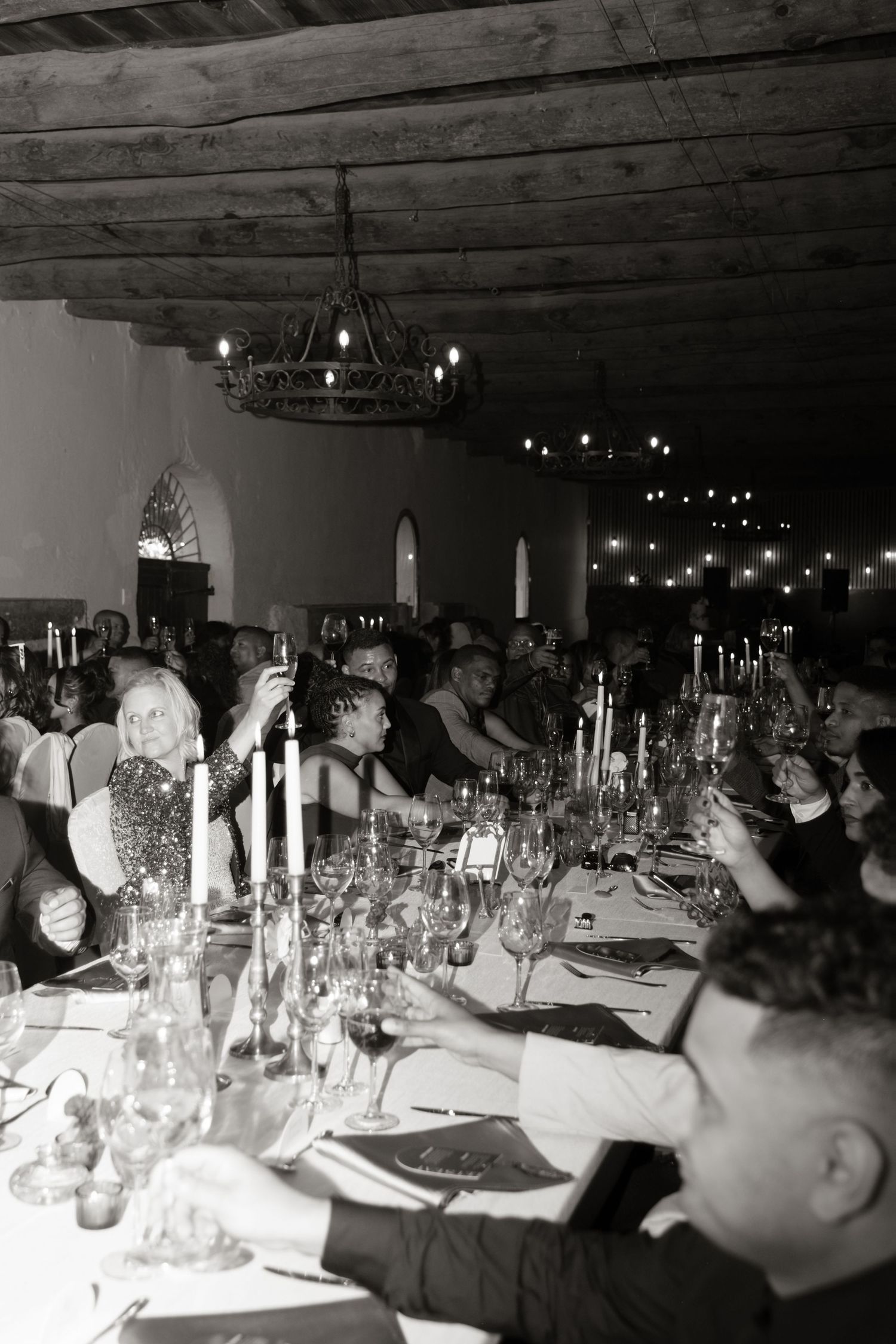Black and white photo of elegant wedding reception dinner with candlelit tables and chandelier lighting.