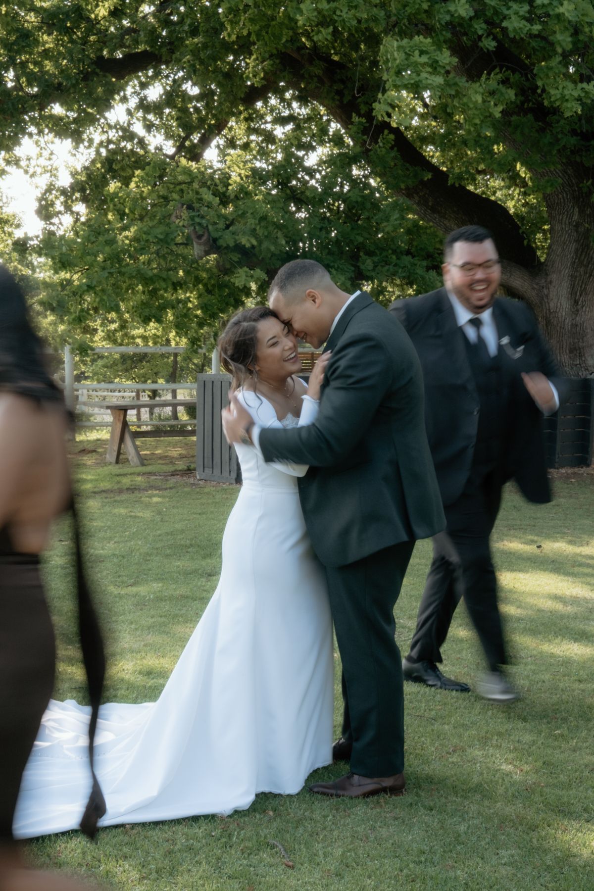 Bride and groom sharing romantic kiss on green lawn surrounded by celebrating wedding guests.