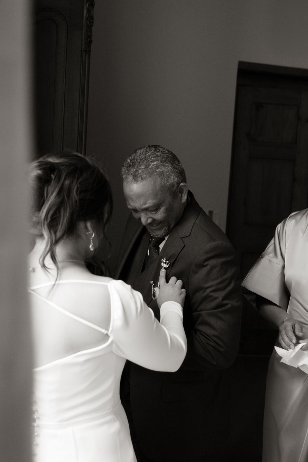 Emotional black and white photo of a bride pinning a boutonniere on her fathers suit jacket before the wedding.