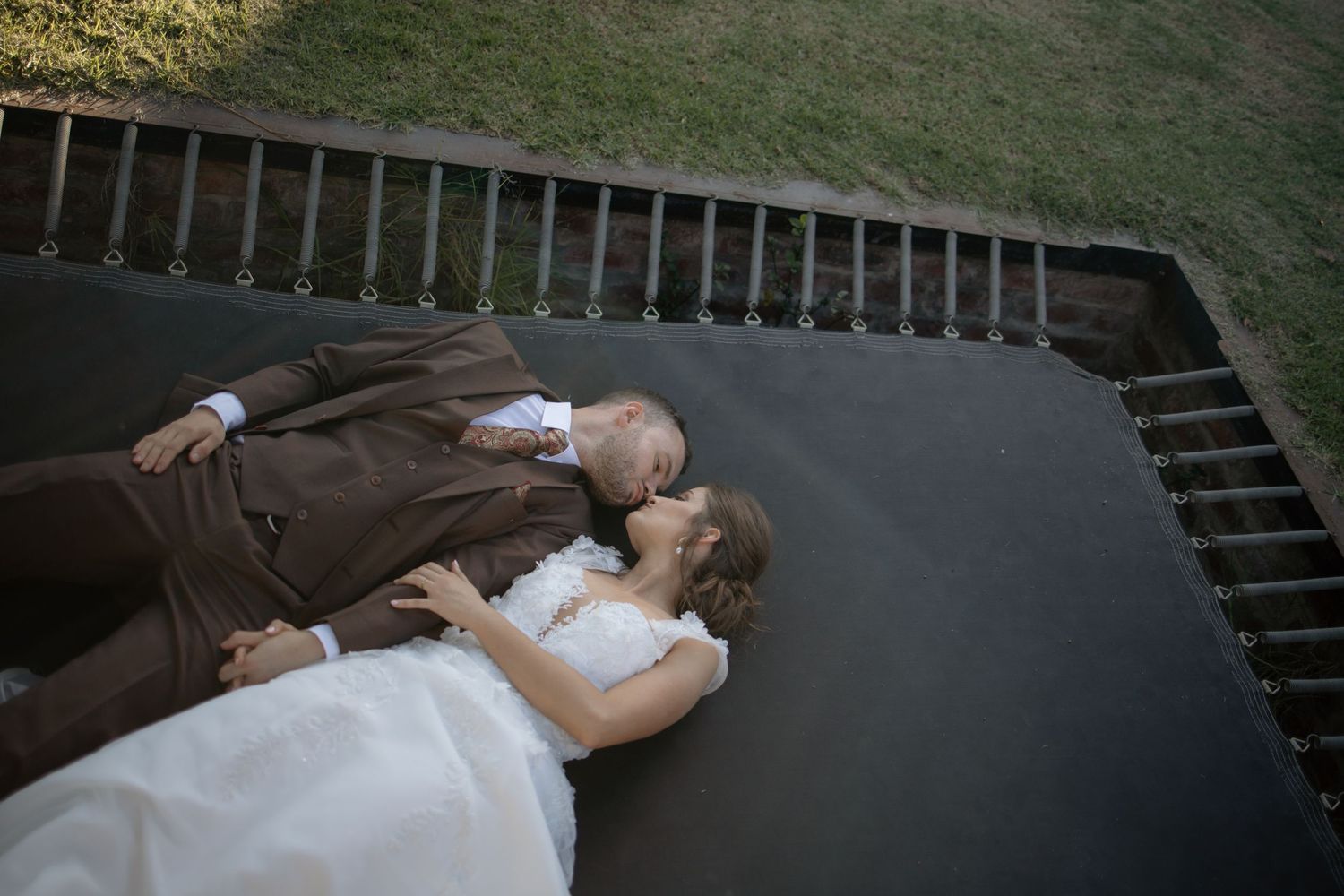 Aerial view of bride and groom lying together on a dark surface in wedding attire.