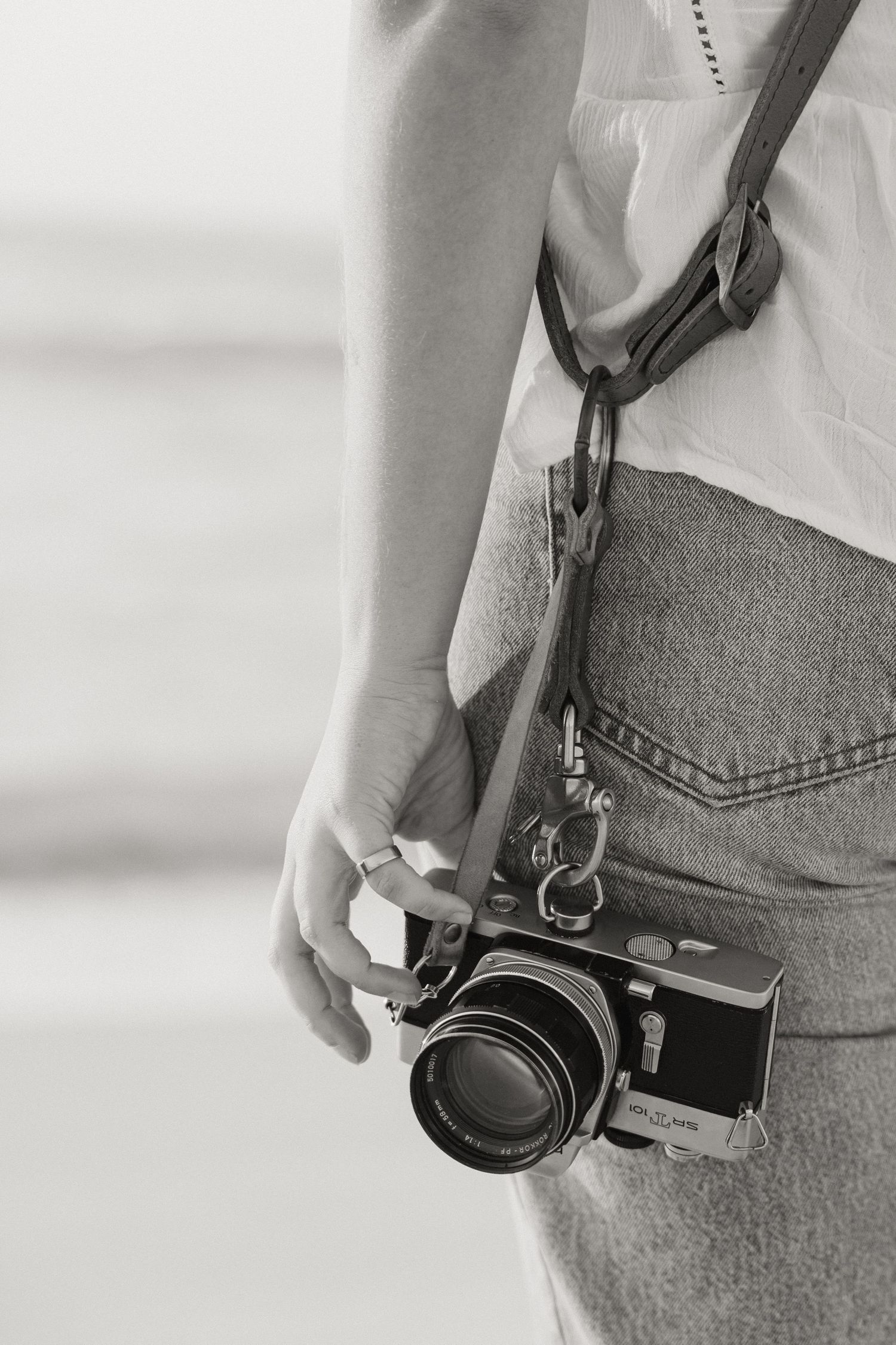 Vintage film camera hanging from leather strap against denim and white clothing.